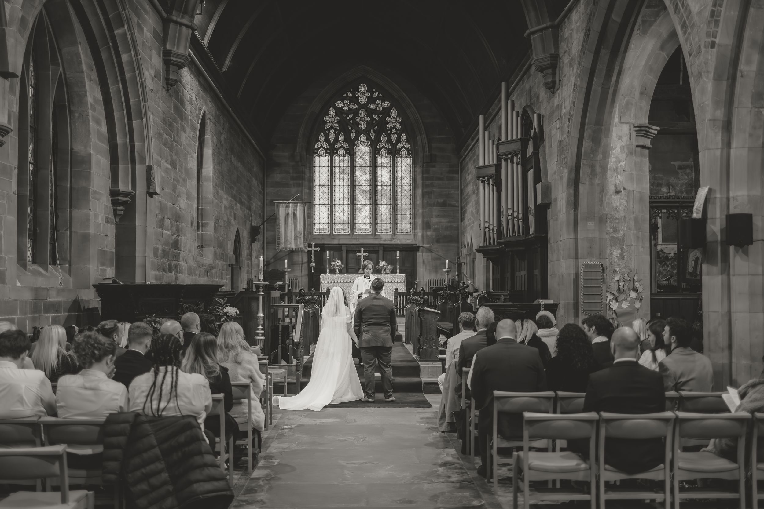 Interior view of a grand cathedral with stone arches and stained glass windows during a ceremony.