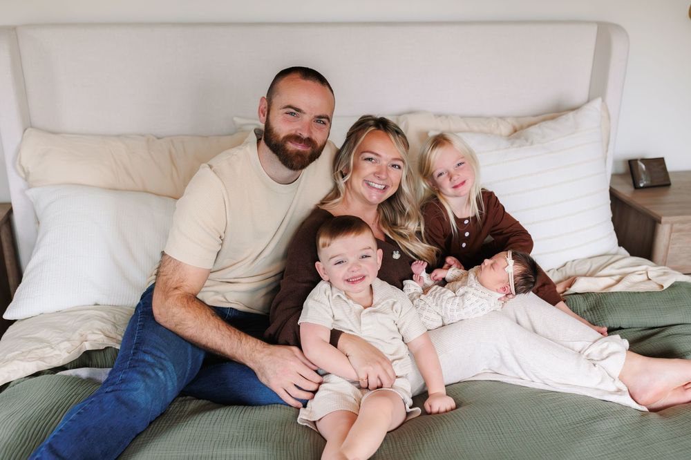 Family relaxing together on a cozy white bed during an intimate lifestyle photoshoot.