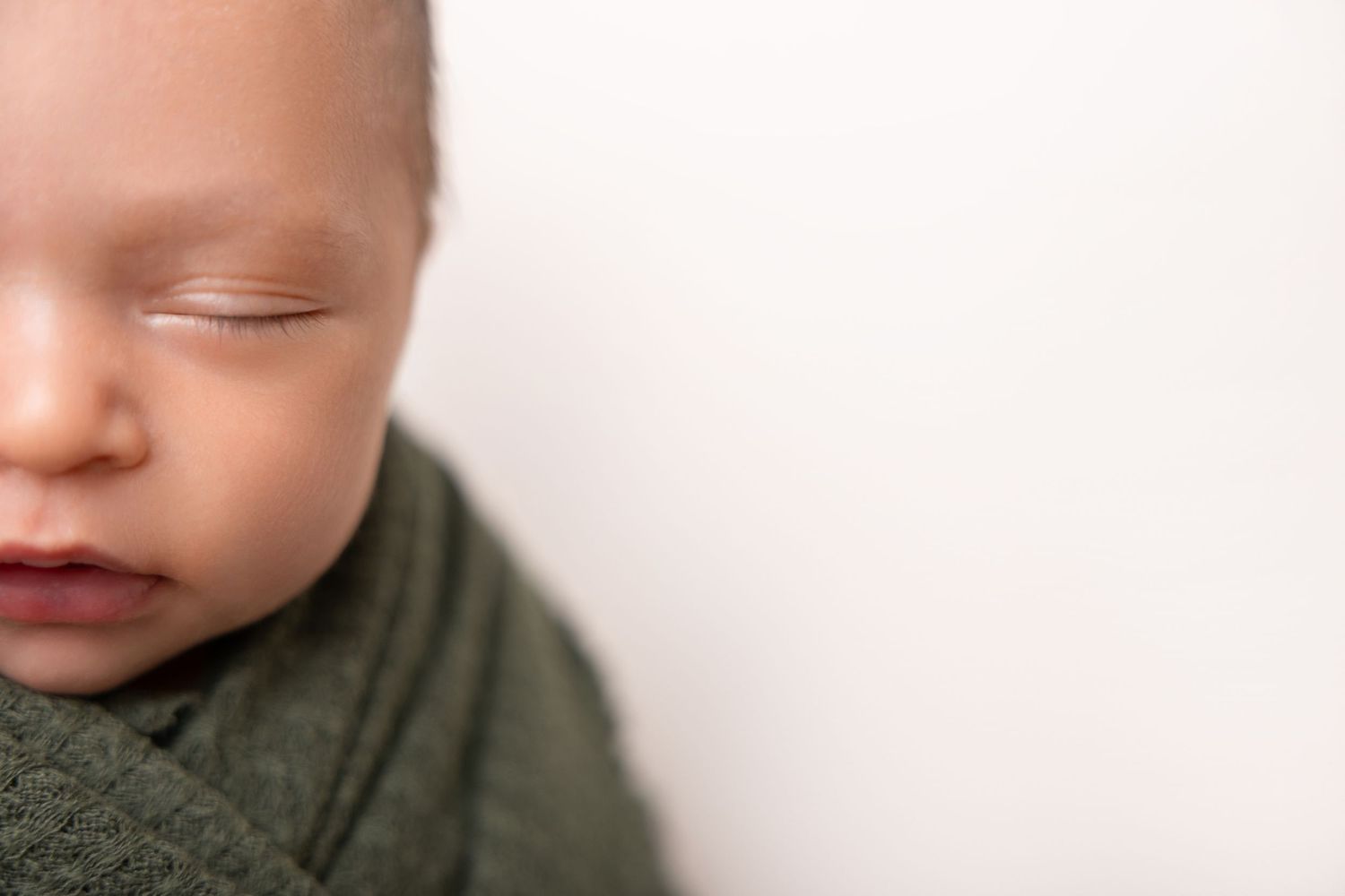 Close-up portrait of a sleeping infant with rosy cheeks against a white background.