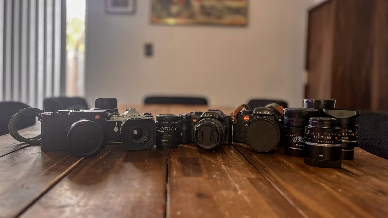 Row of professional cameras and lenses arranged on rustic wooden surface.