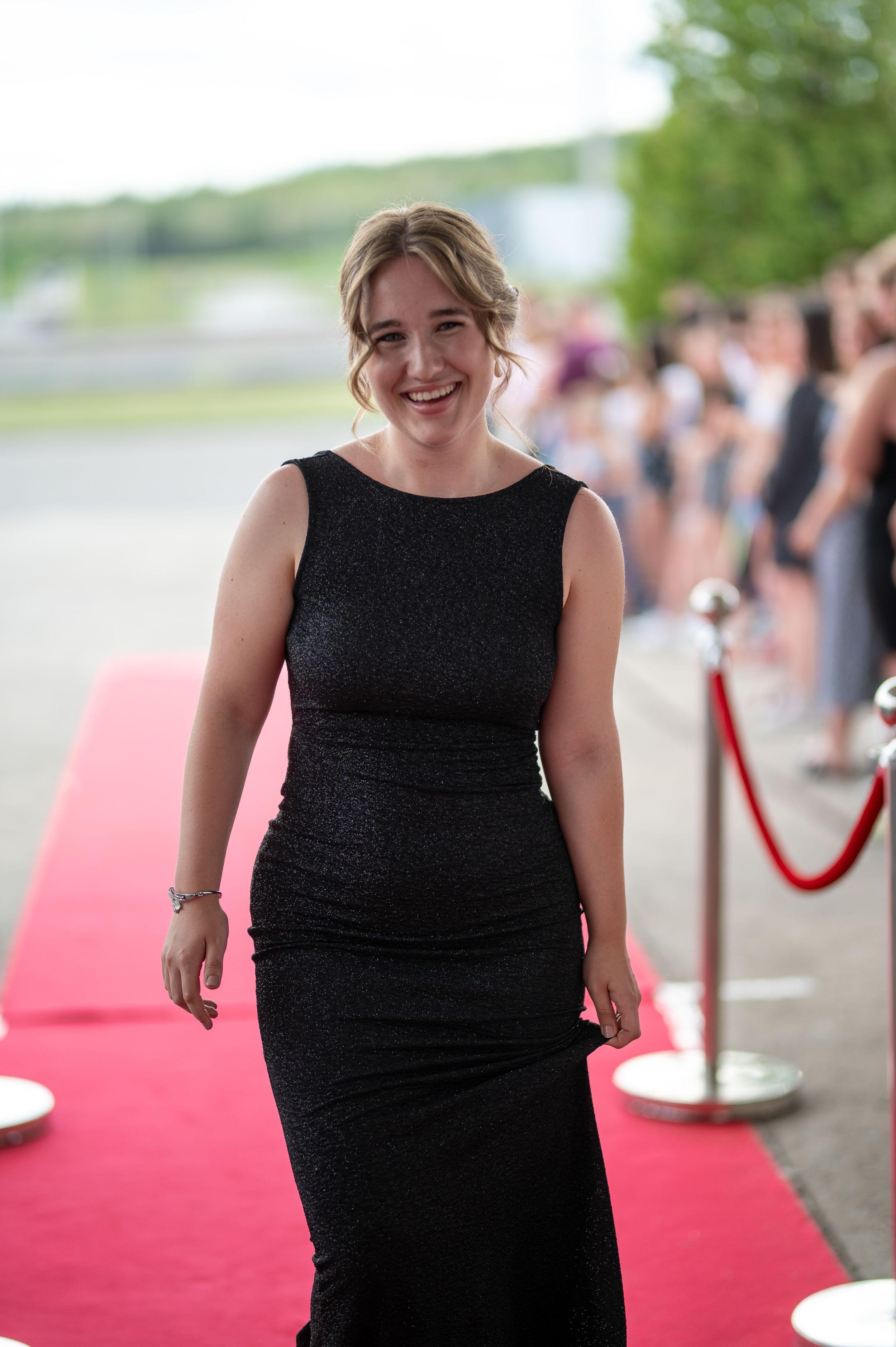 Person in a fitted black formal dress walks along a red carpet at an event.