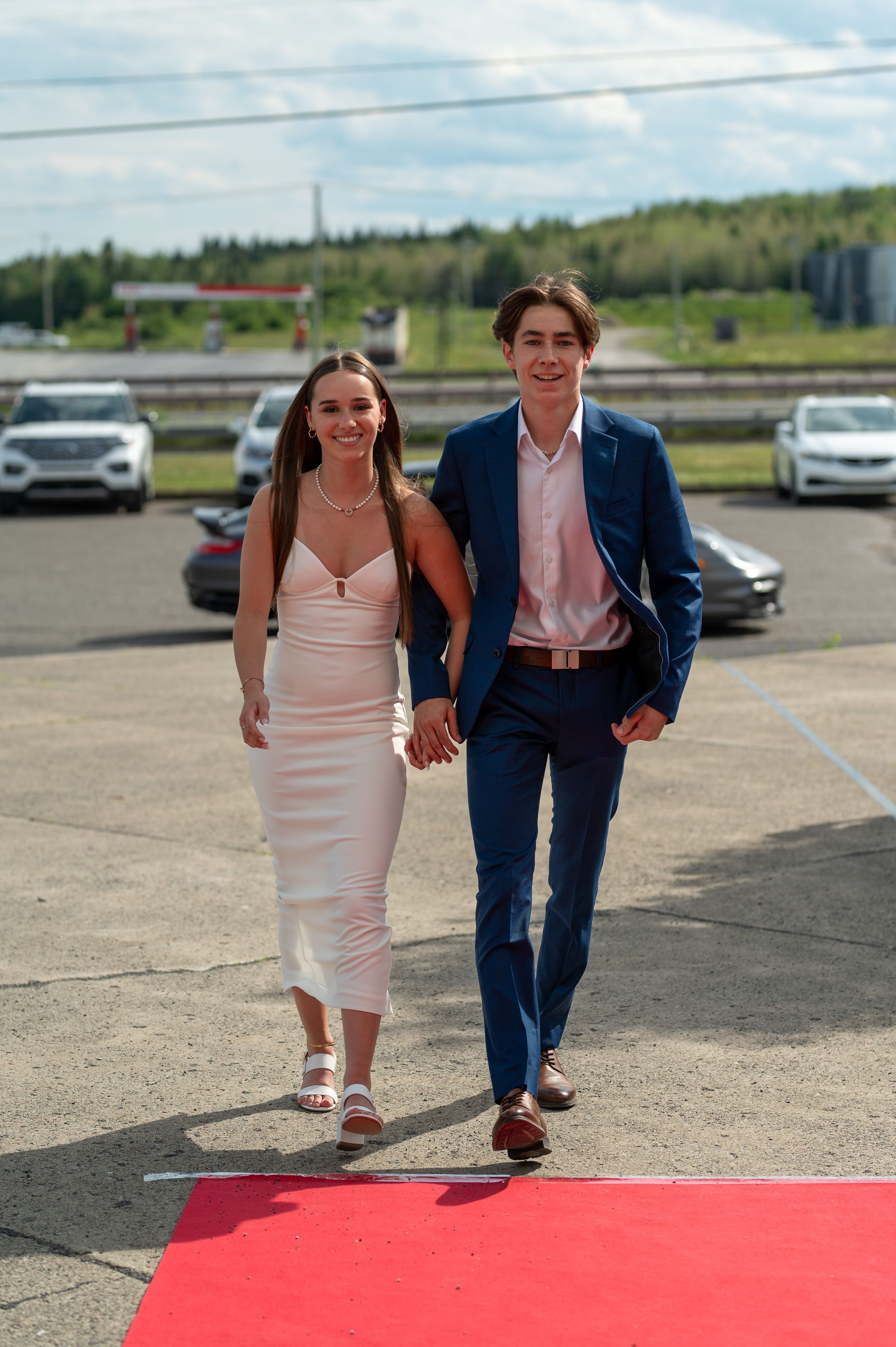 Couple walks hand in hand on red carpet, wearing formal attire.