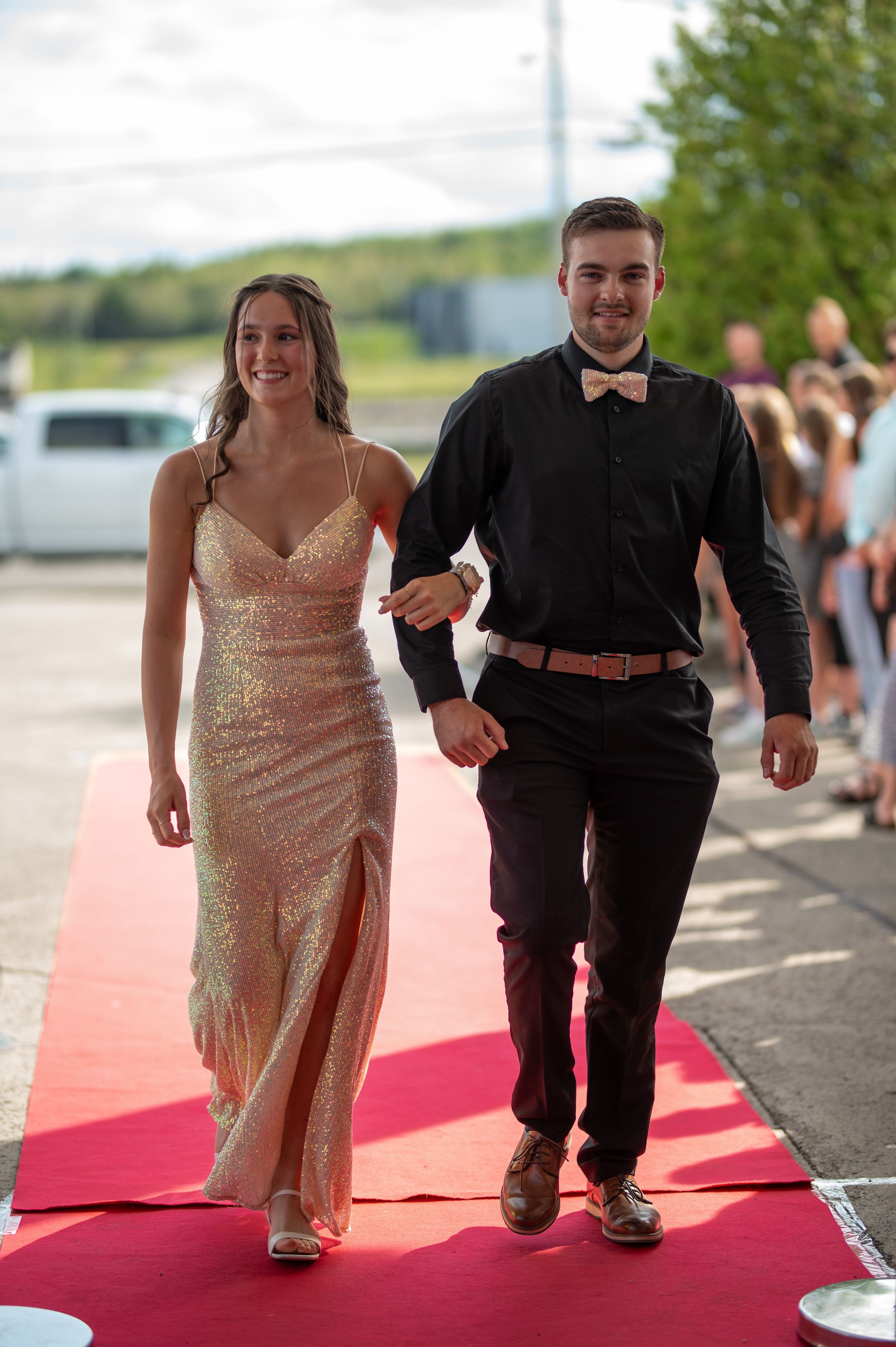 Couple walks arm in arm on red carpet, one wearing sparkly gold dress.