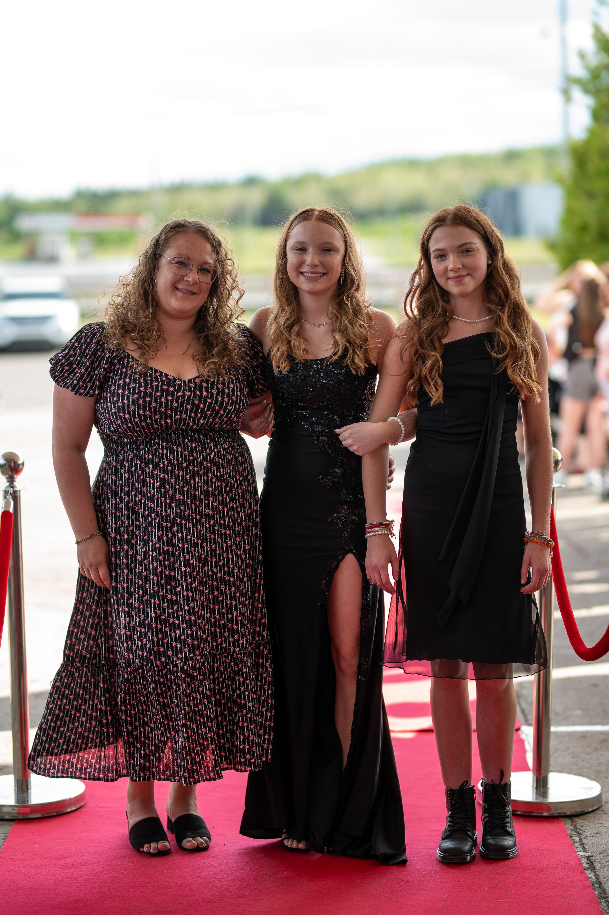 Three women pose on a red carpet in formal dresses at an event.