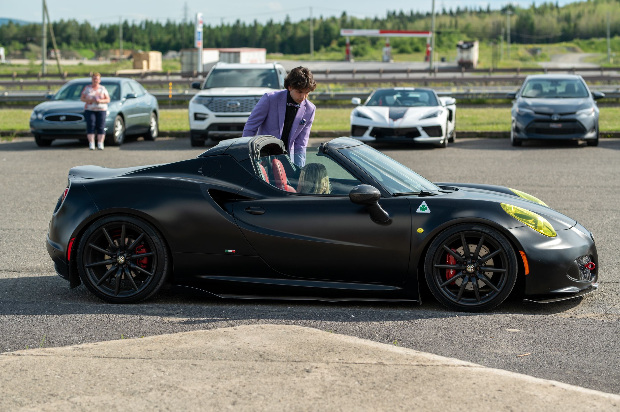 A sleek black sports car parked in a lot with someone sitting in the driver's seat.