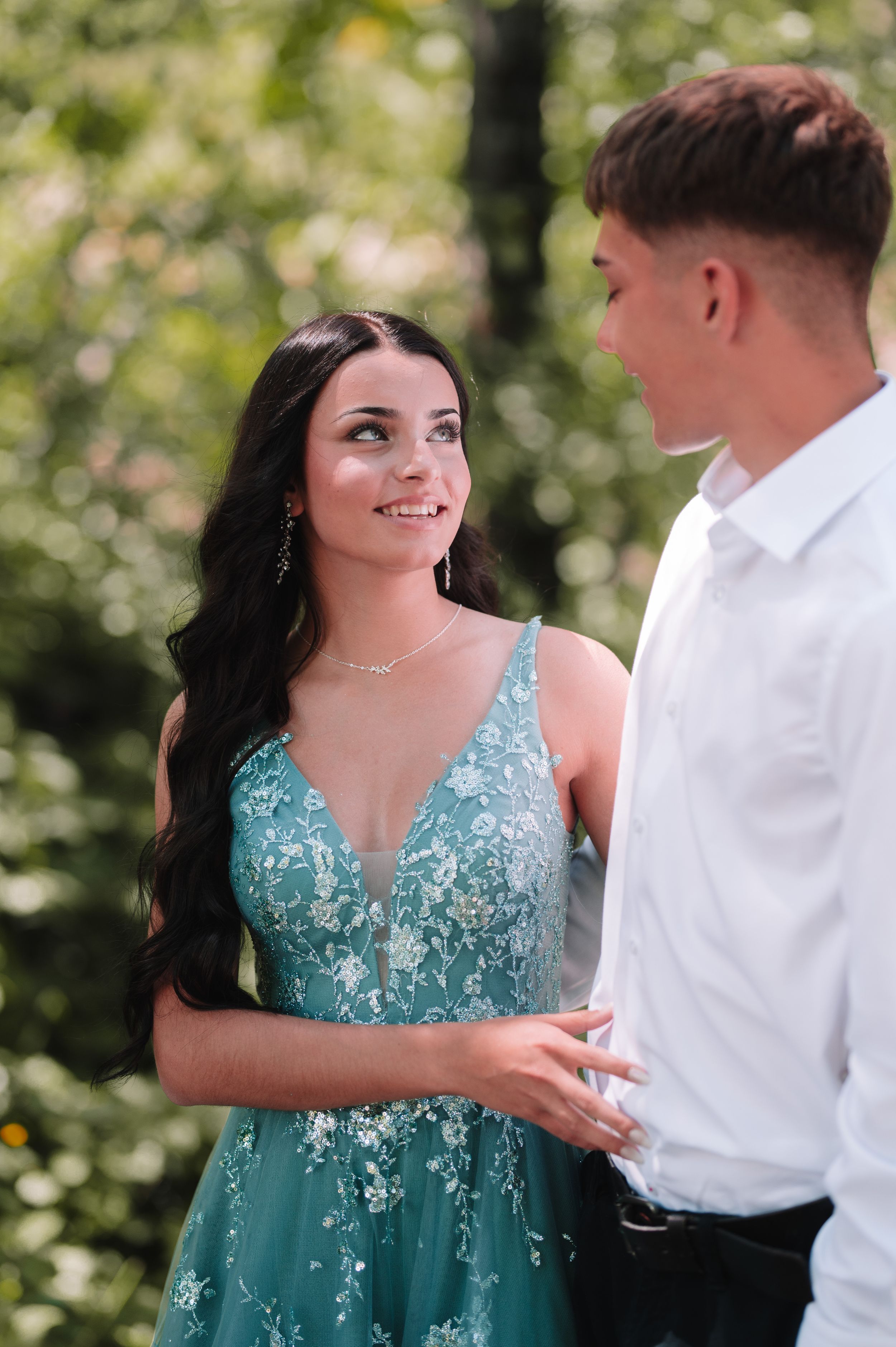 Couple in formal attire shares romantic moment in sunlit garden setting.