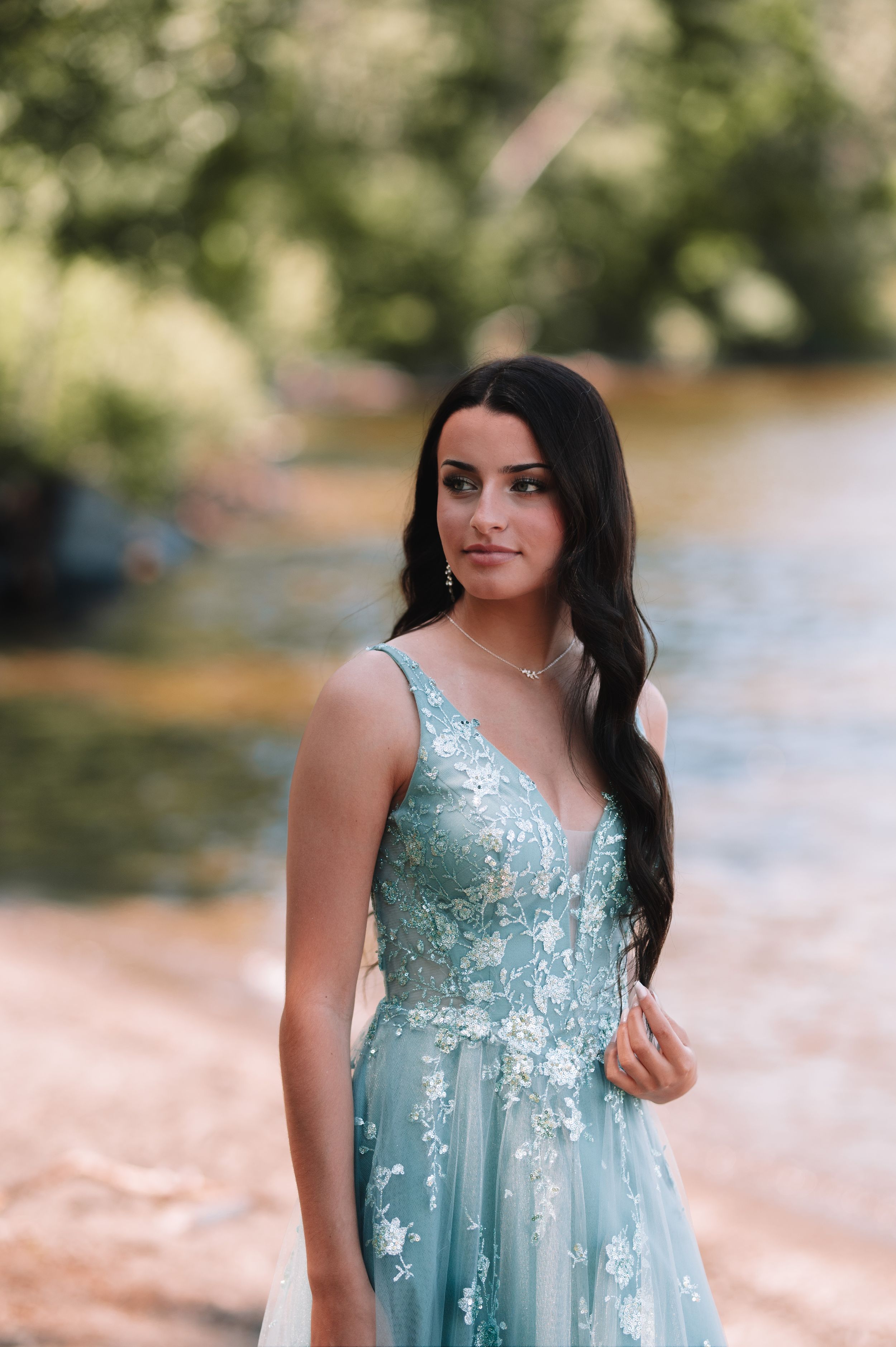 Elegant portrait featuring flowing turquoise gown with lace details in natural setting.