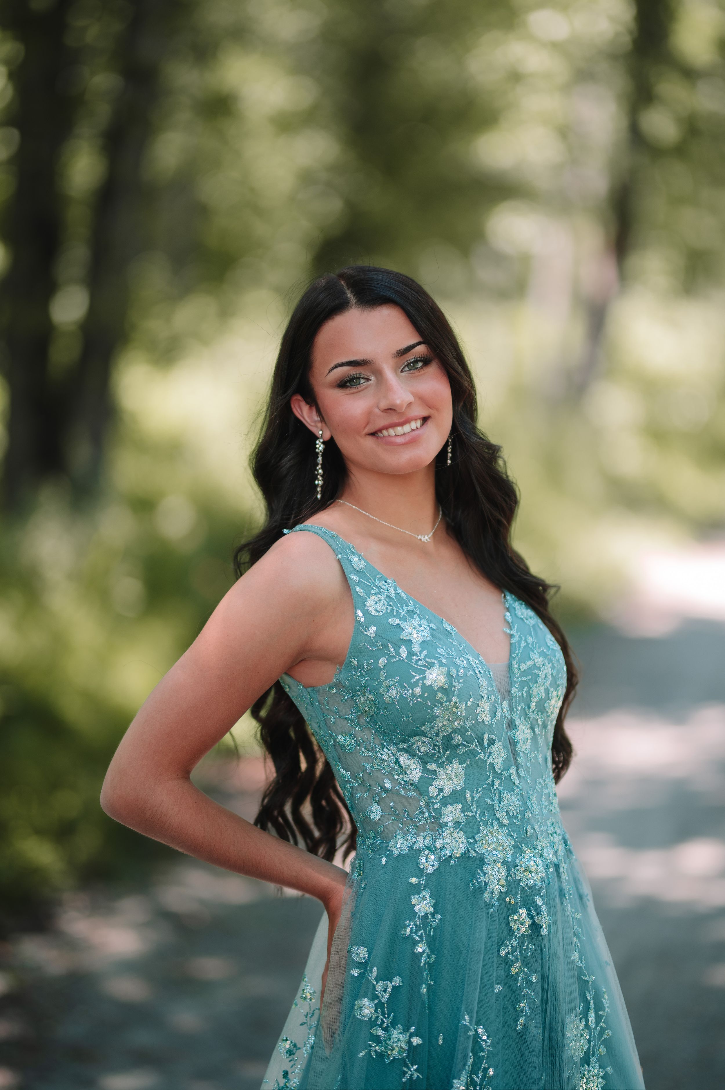 Portrait of woman in turquoise embellished gown amid forest greenery.