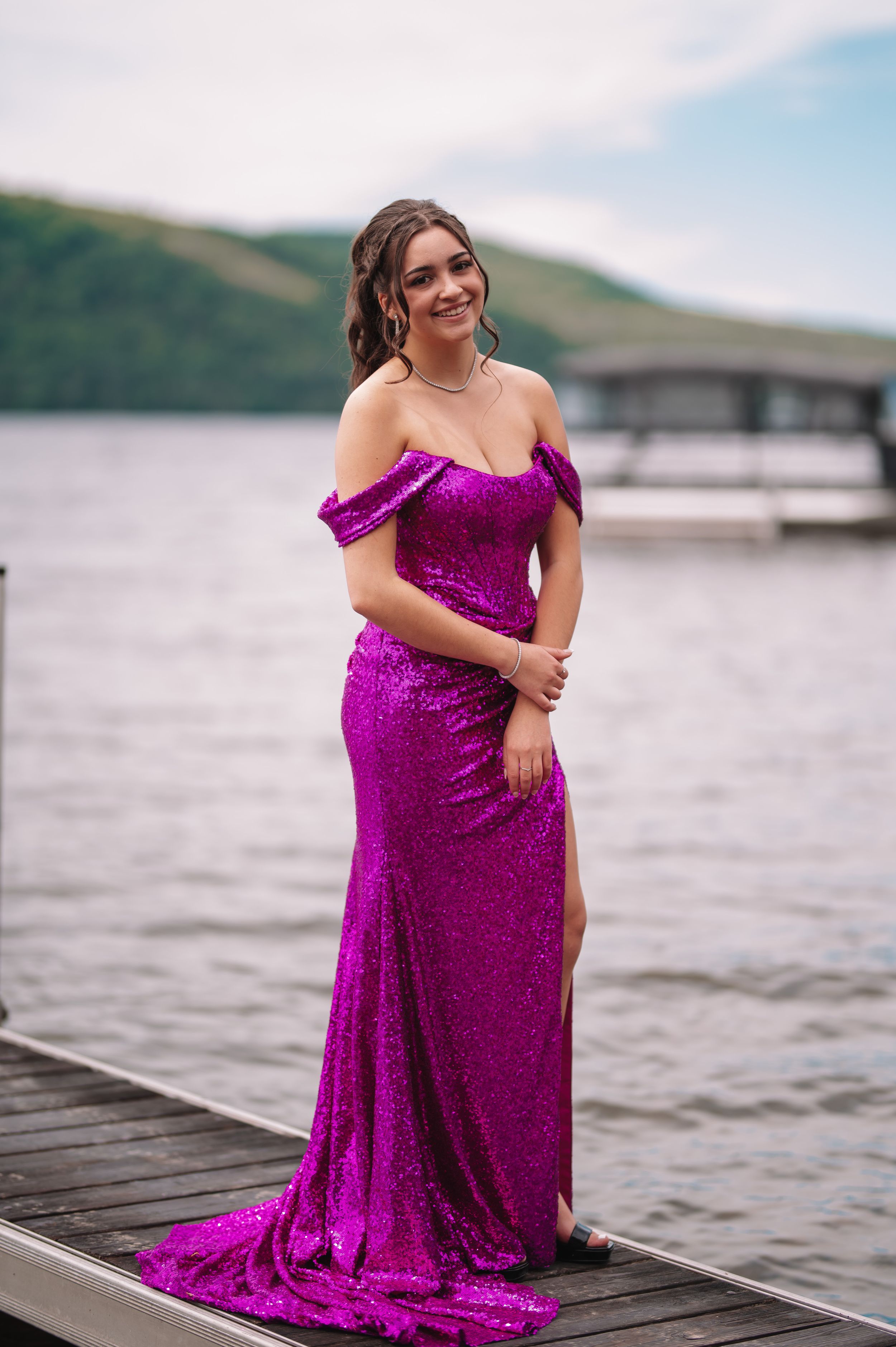 A sequined fuchsia off-shoulder gown worn on a dock overlooking a lake.