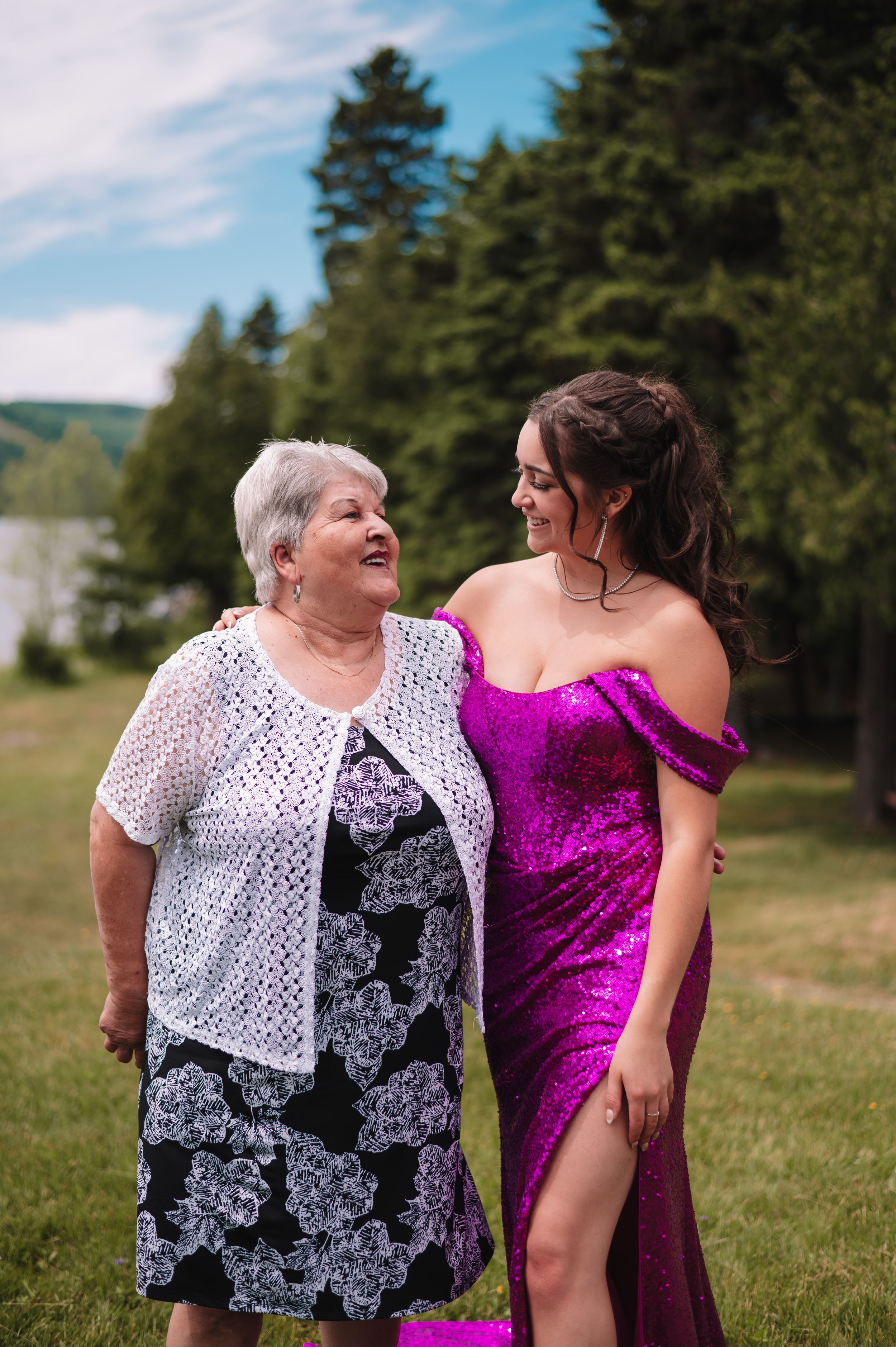 A warm moment captured outdoors between two people in contrasting white lace and magenta sequin dresses.