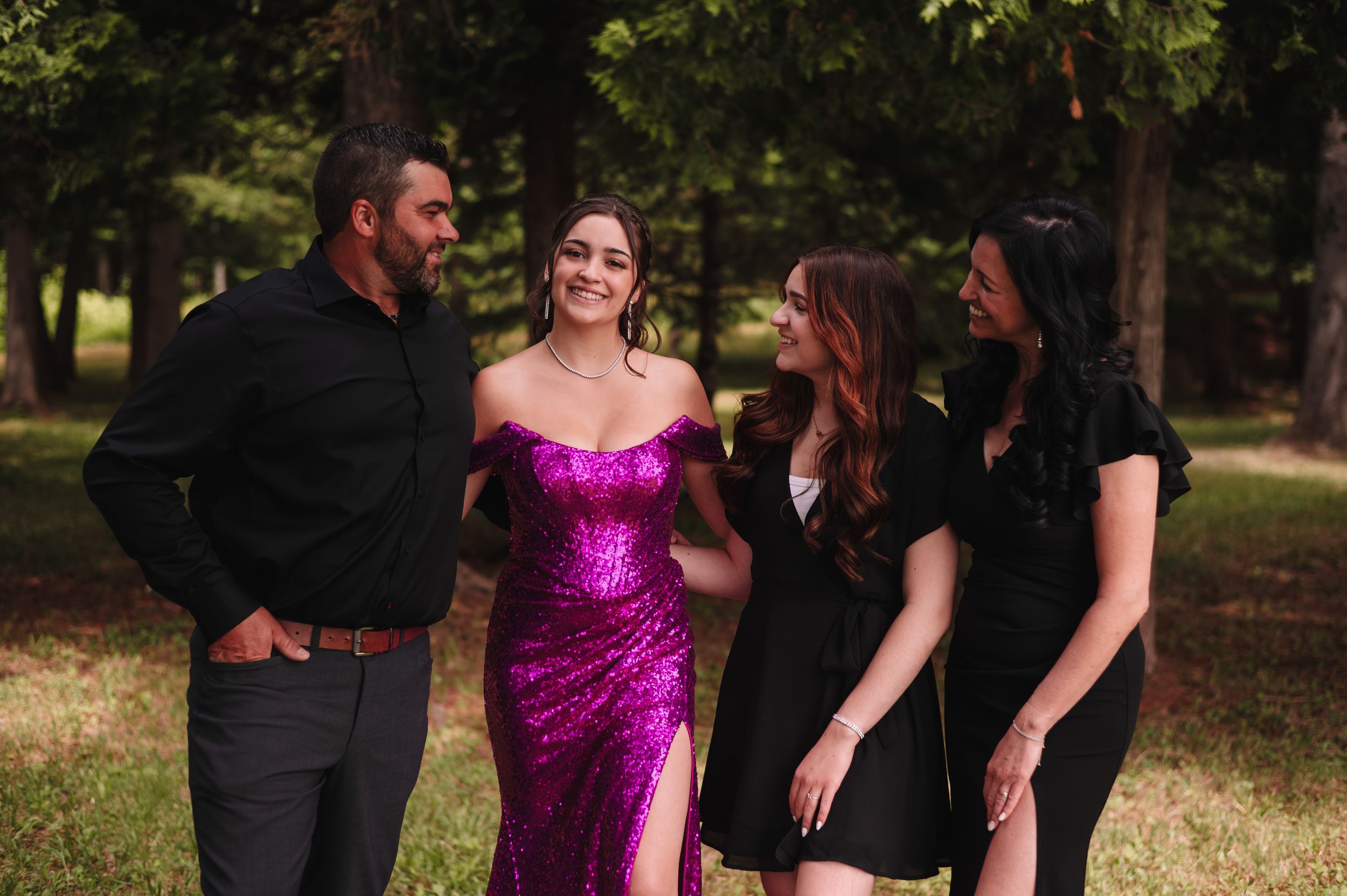 A group photo featuring a bright pink formal dress and casual black attire in an outdoor setting.