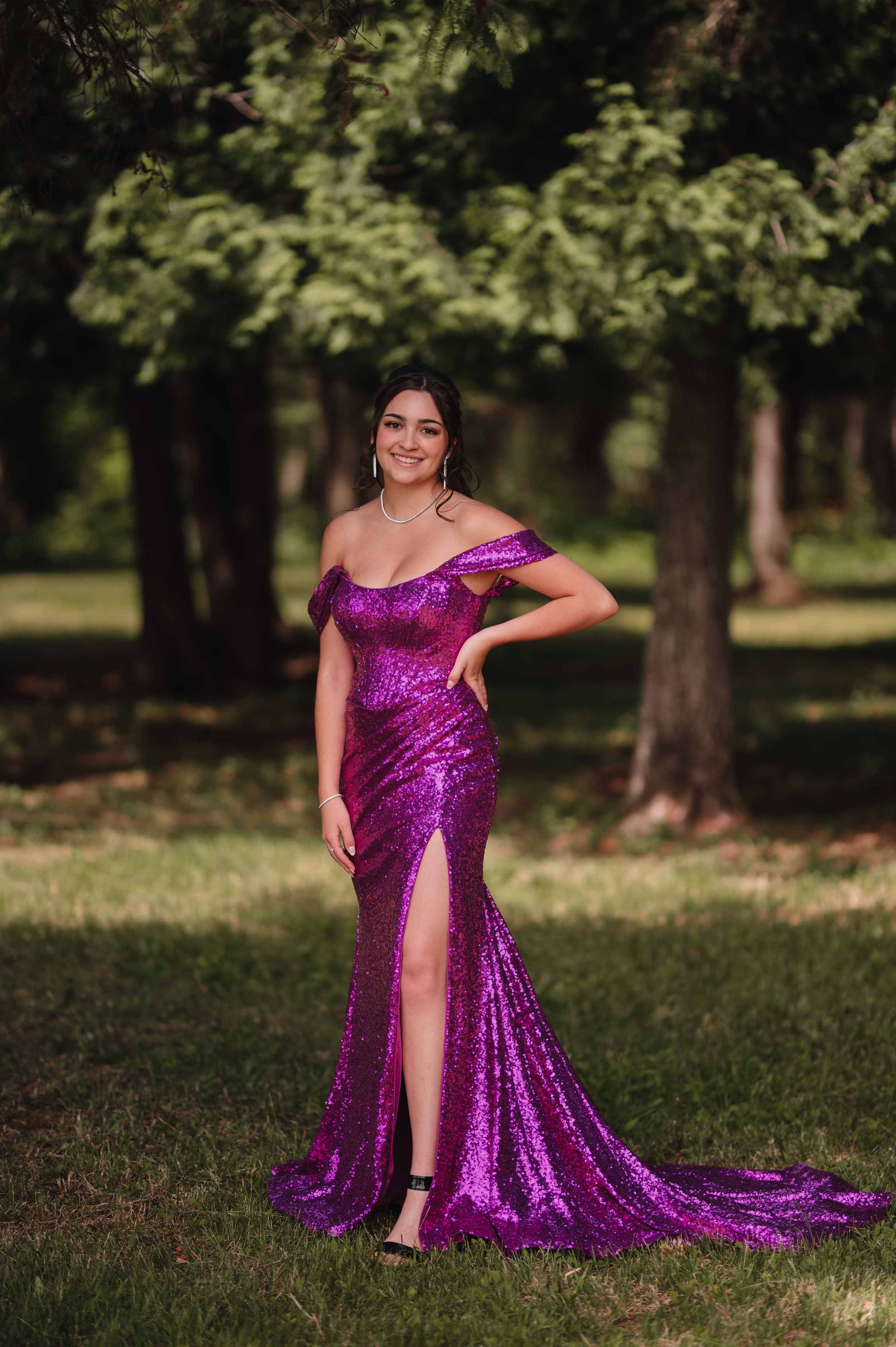 A sequined magenta formal dress with a side slit photographed in a wooded park setting.