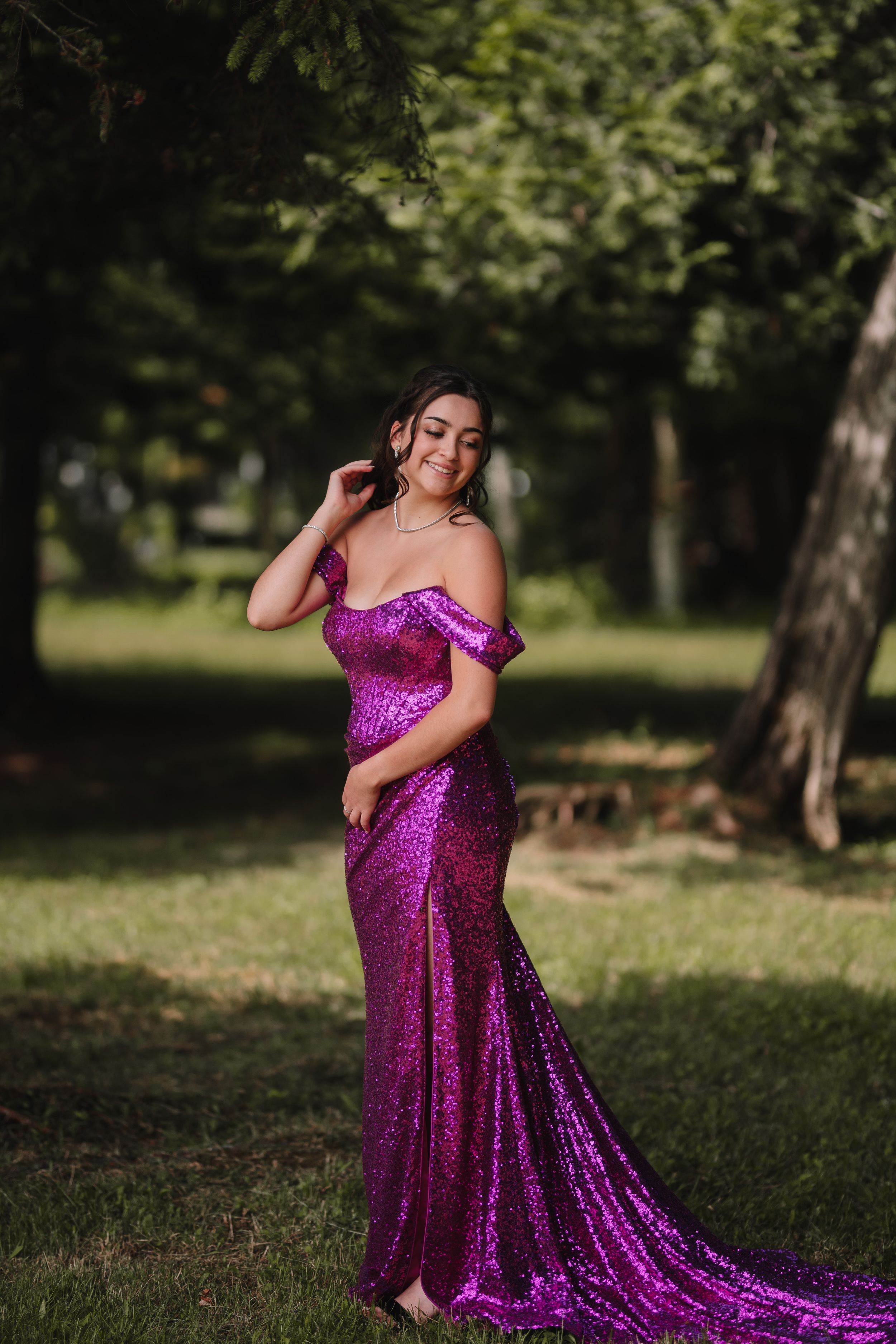 A flowing magenta sequin gown with off-shoulder detail photographed in a park setting.