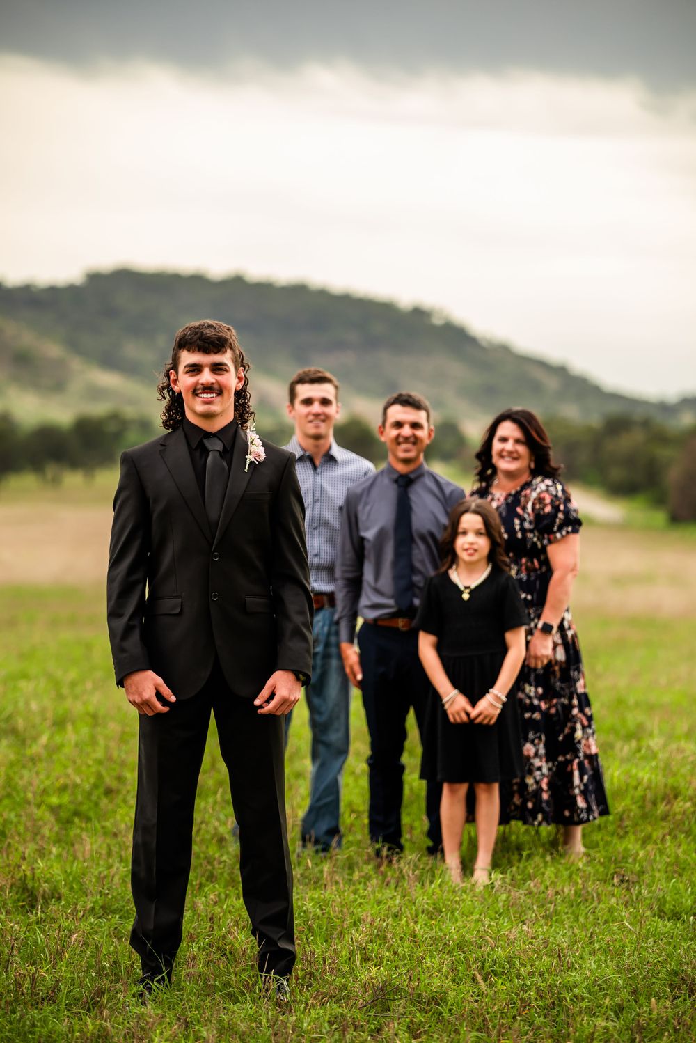 Formal family portrait of five people standing in a rural field setting.