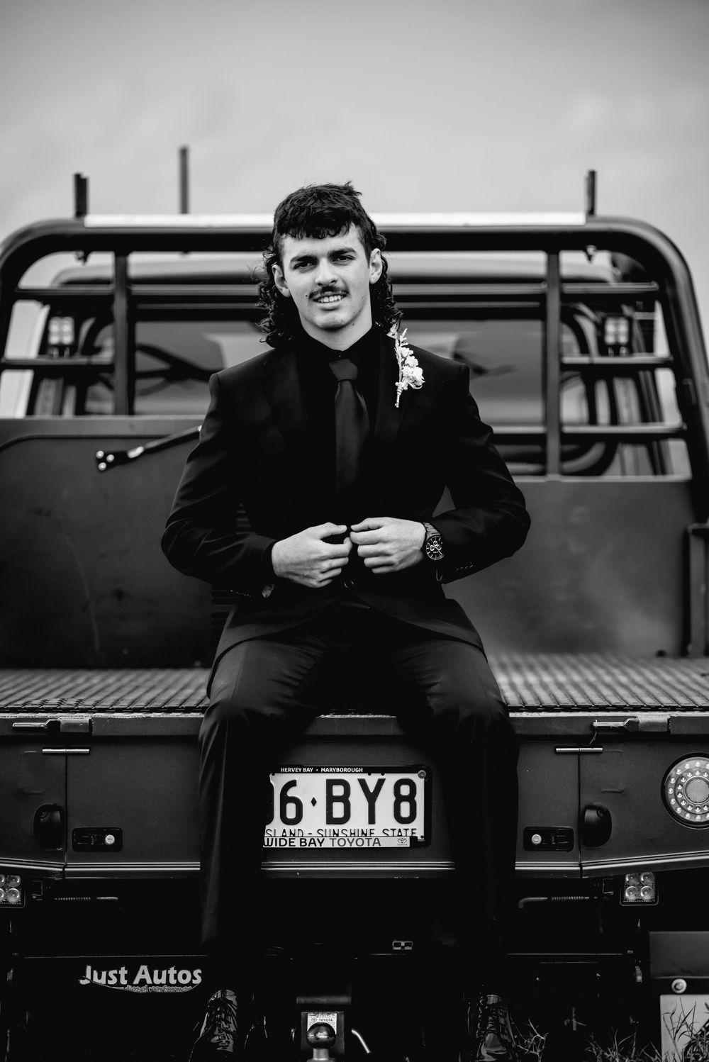 Person in black suit sitting on vintage truck bed with visible license plate.