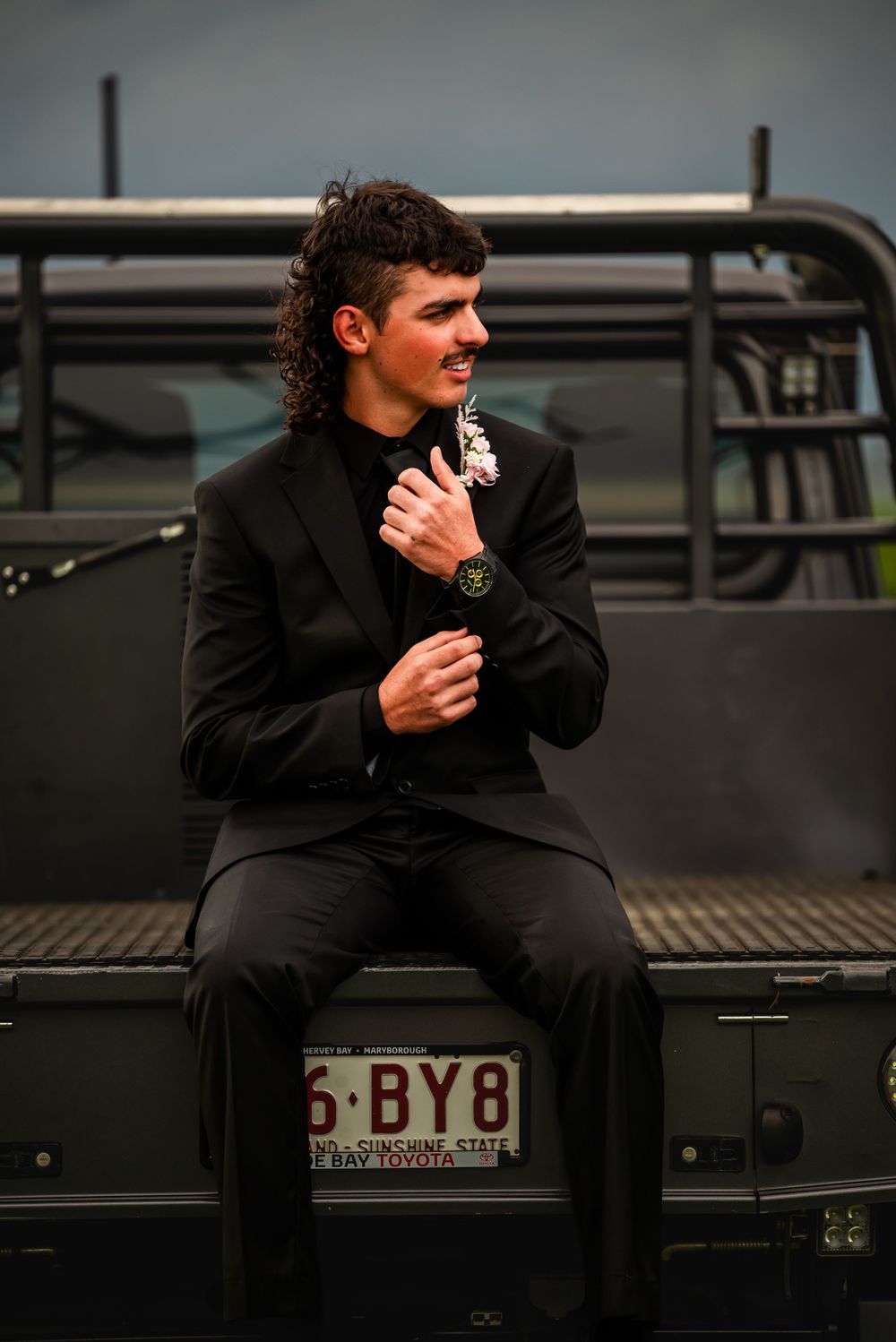 Person in formal attire sitting on vintage truck bed adjusting cuffs.