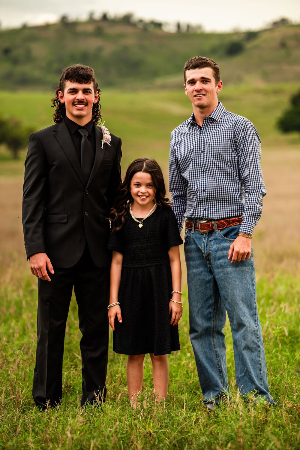 Three people posing together in field with formal and casual attire.