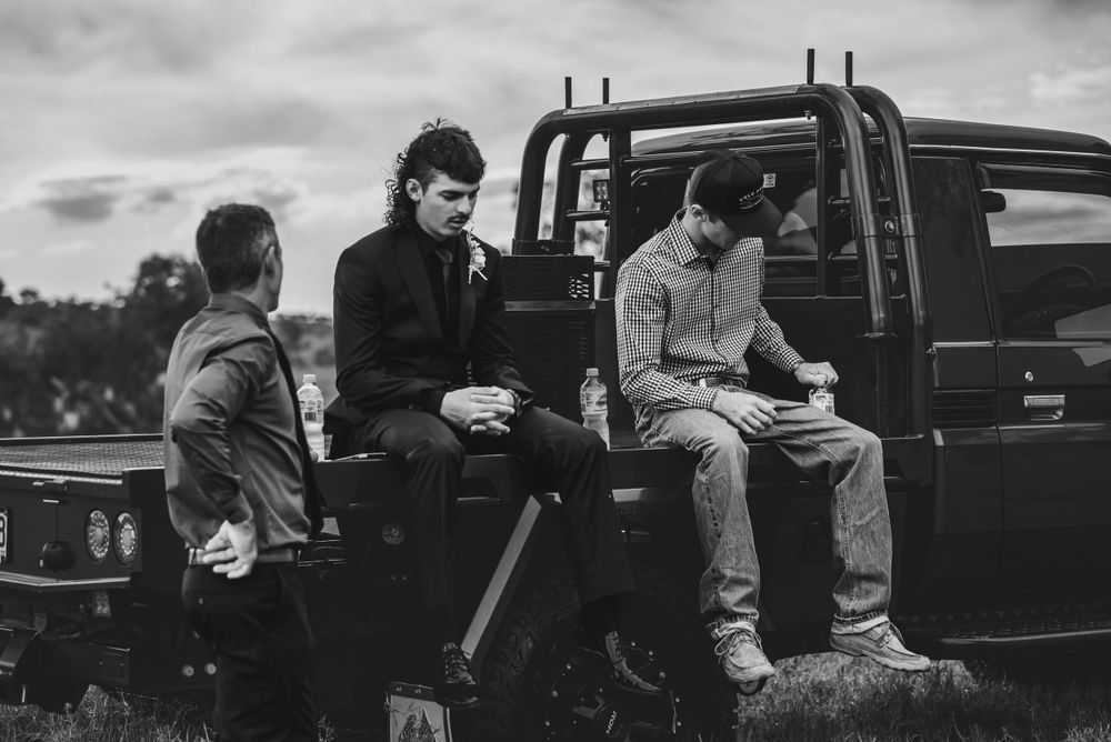 Three friends relaxing casually on the bed of a pickup truck in black and white.