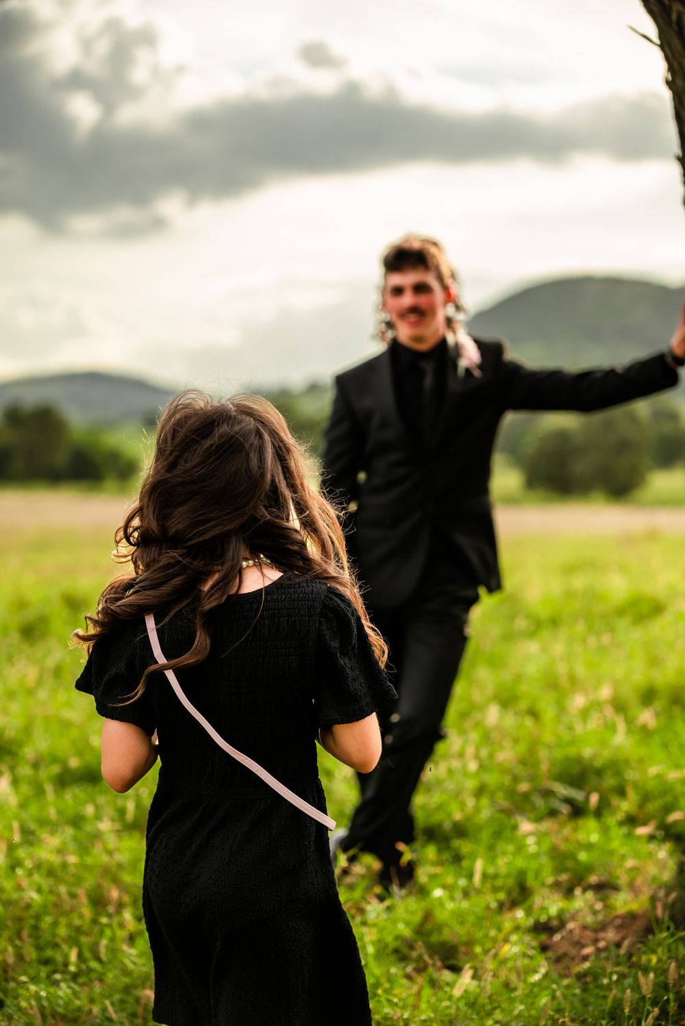Two people enjoying a playful moment in a grassy field with mountains in the background.
