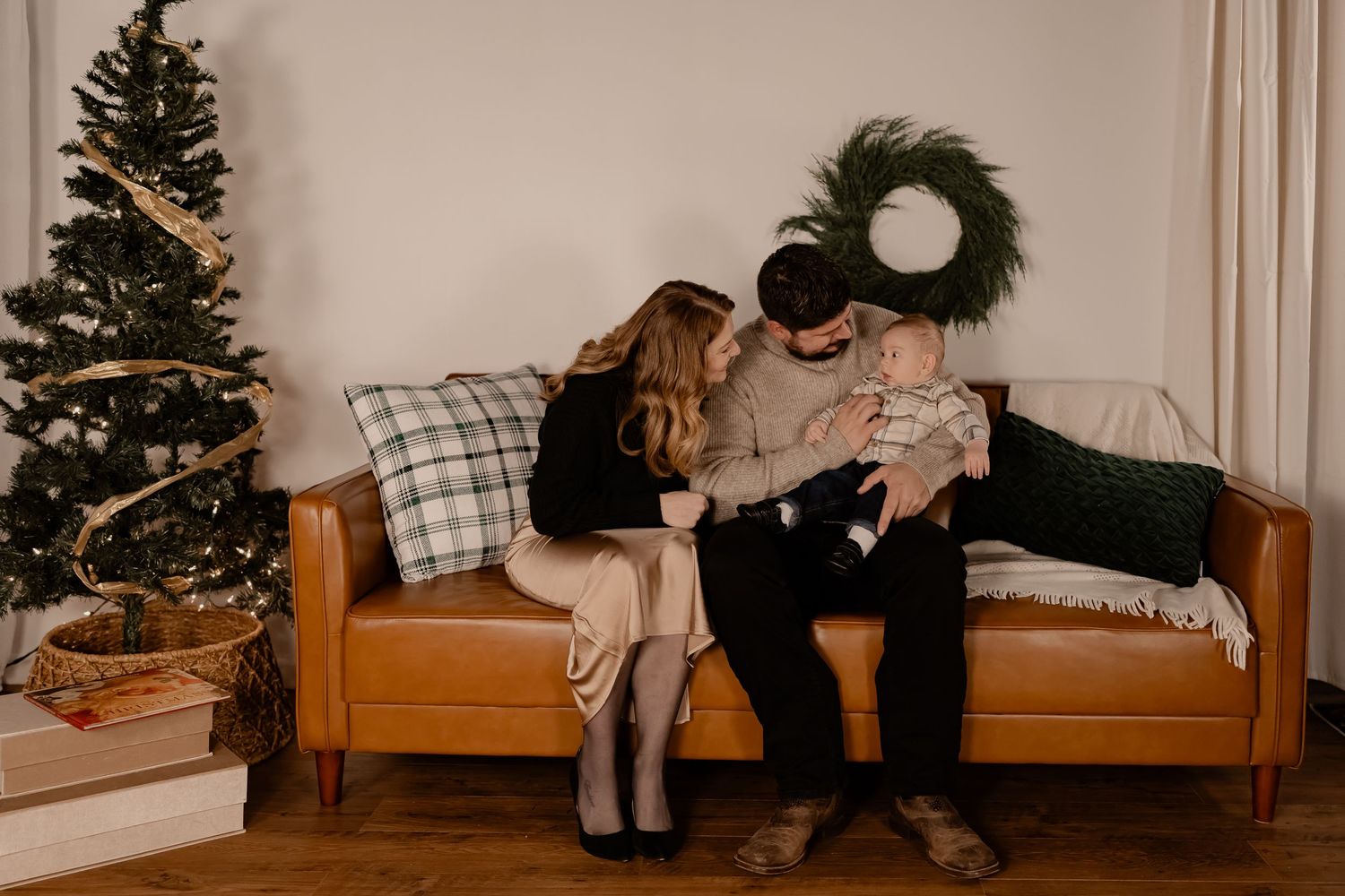 Intimate family holiday moment on a brown leather couch next to a Christmas tree in a cozy living room.
