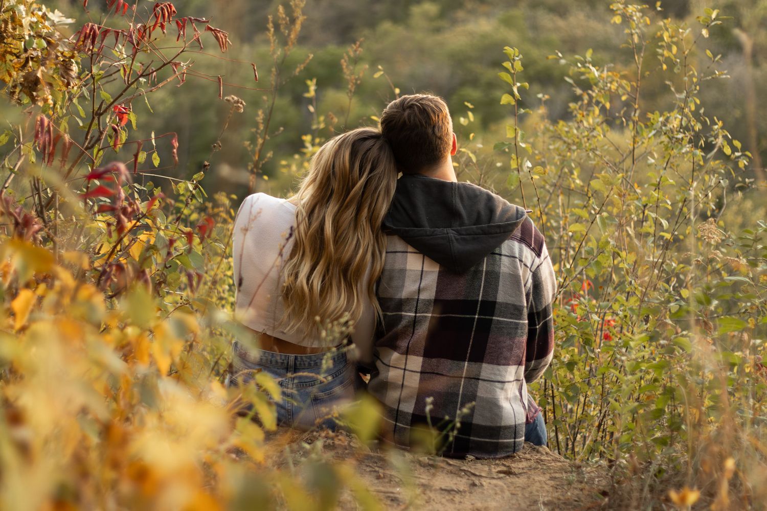Two people sitting together among tall wildflowers during golden hour in nature.