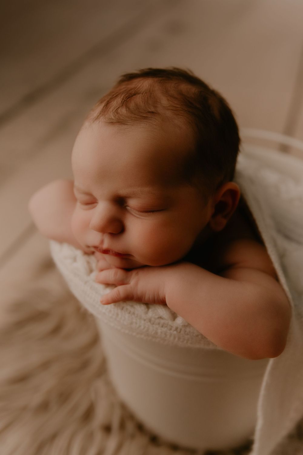 Peaceful sleeping newborn rests on soft white blankets in warm lighting.