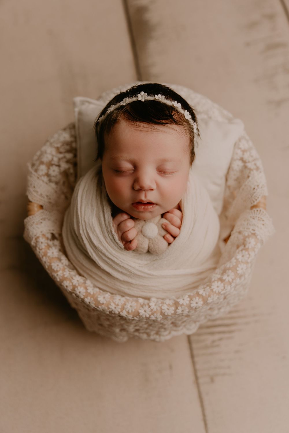 Sleeping newborn baby wrapped in white fabric nestled in lace doily photographed from above in sepia tones.