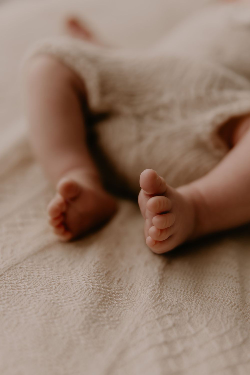 Close-up view of tiny baby feet resting on a soft beige blanket in a row showing different angles.