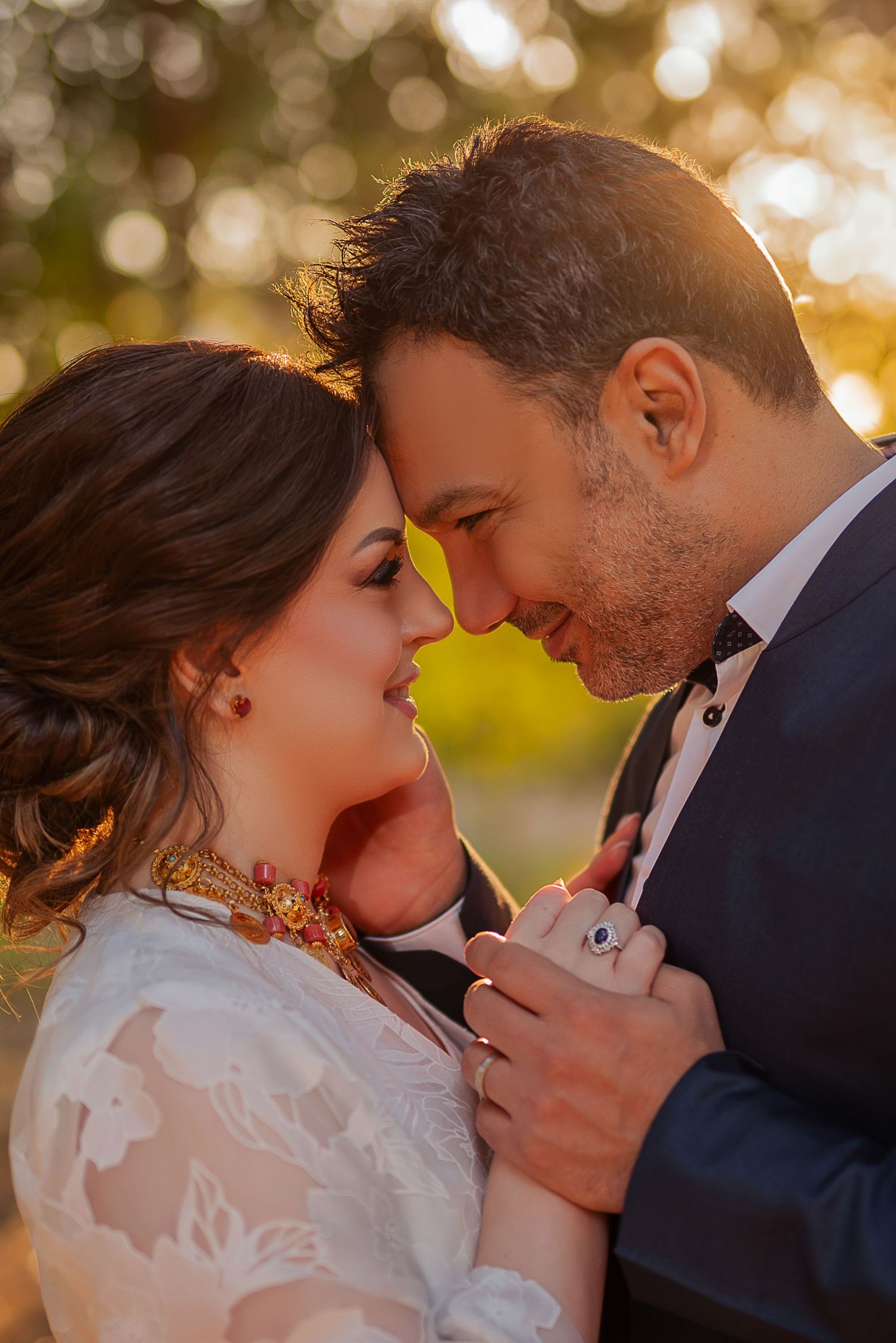 A romantic wedding portrait with the couple in tender embrace at sunset with golden bokeh lighting in the background.