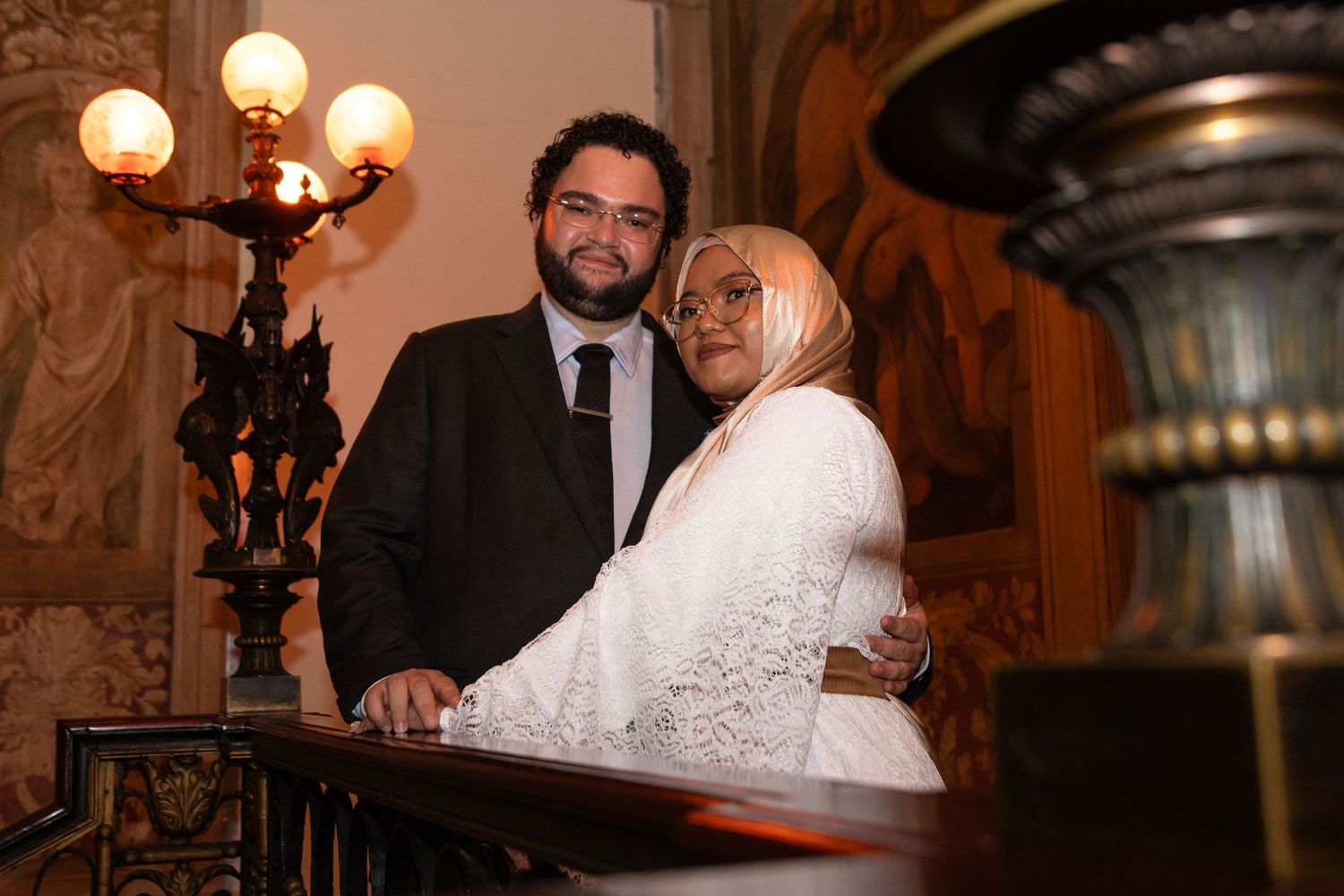 Elegant wedding couple dancing under vintage chandeliers in historic venue.
