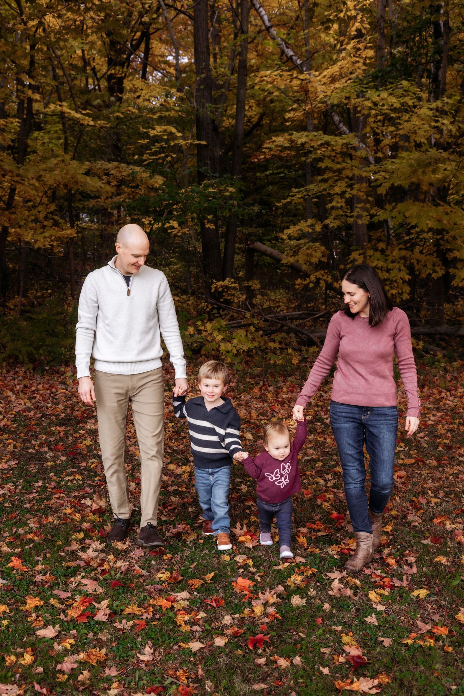 Family walks together on autumn trail with white dog and falling leaves.