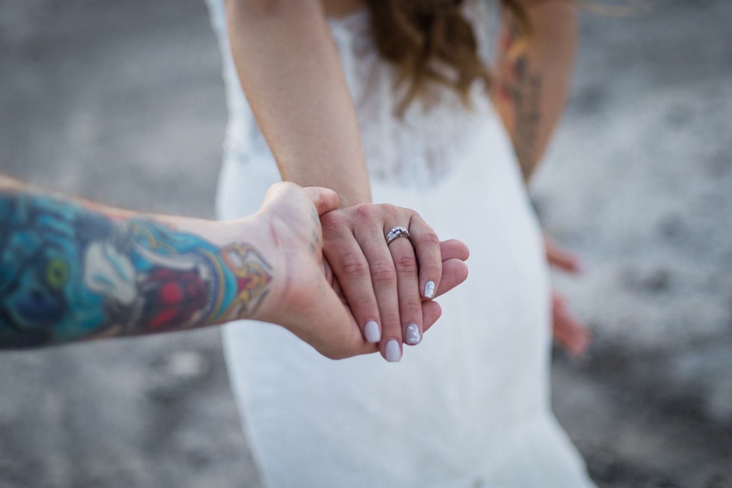 Close-up of hands with wedding rings and colorful tattoo against a blurred background.