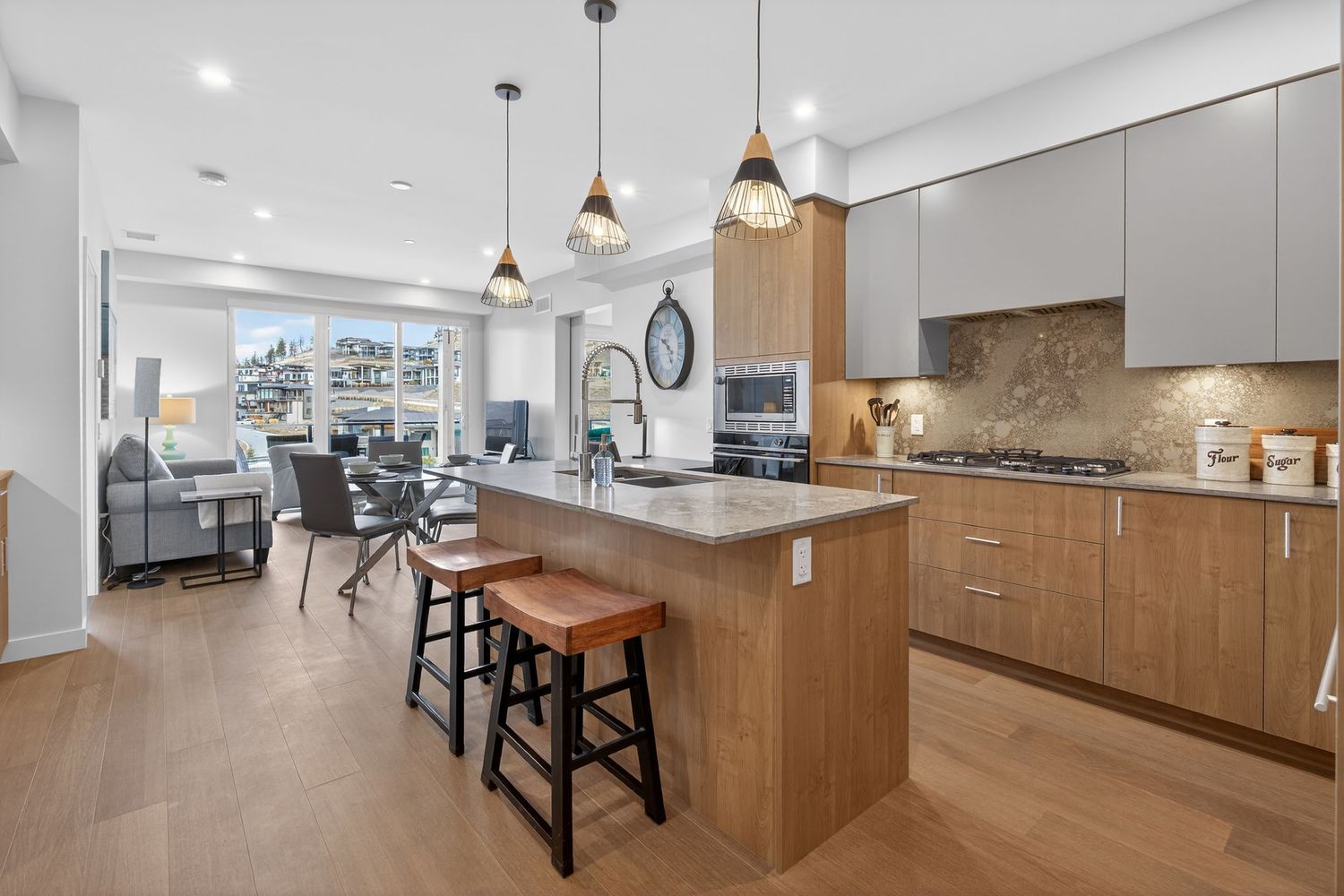 Modern open concept kitchen and living area with wood paneling, pendant lights, and sleek white cabinetry.