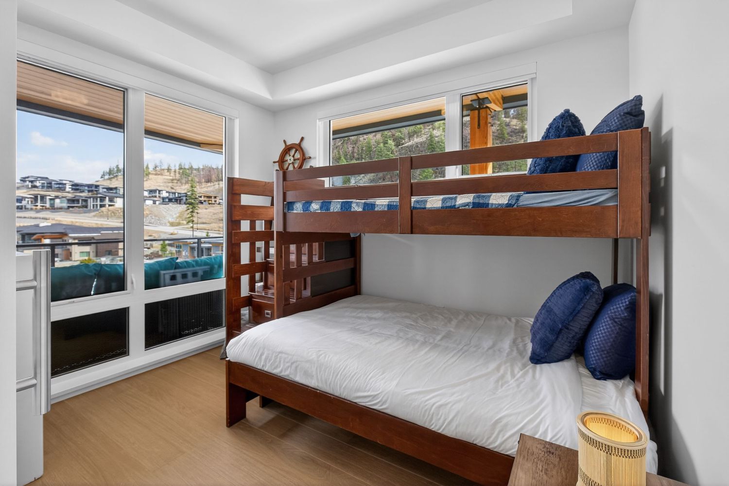 Modern bedroom with wooden bunk bed, navy blue pillows, hardwood floors, and large windows with marina views.
