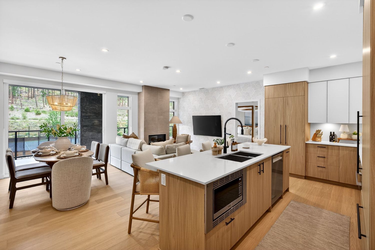 Modern open-concept kitchen with wood cabinetry, white quartz island, and dining area with floor-to-ceiling windows.