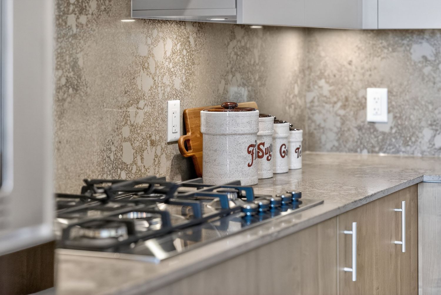 Modern kitchen interior with concrete walls, stainless steel appliances, and white cabinets features a sleek minimalist design.
