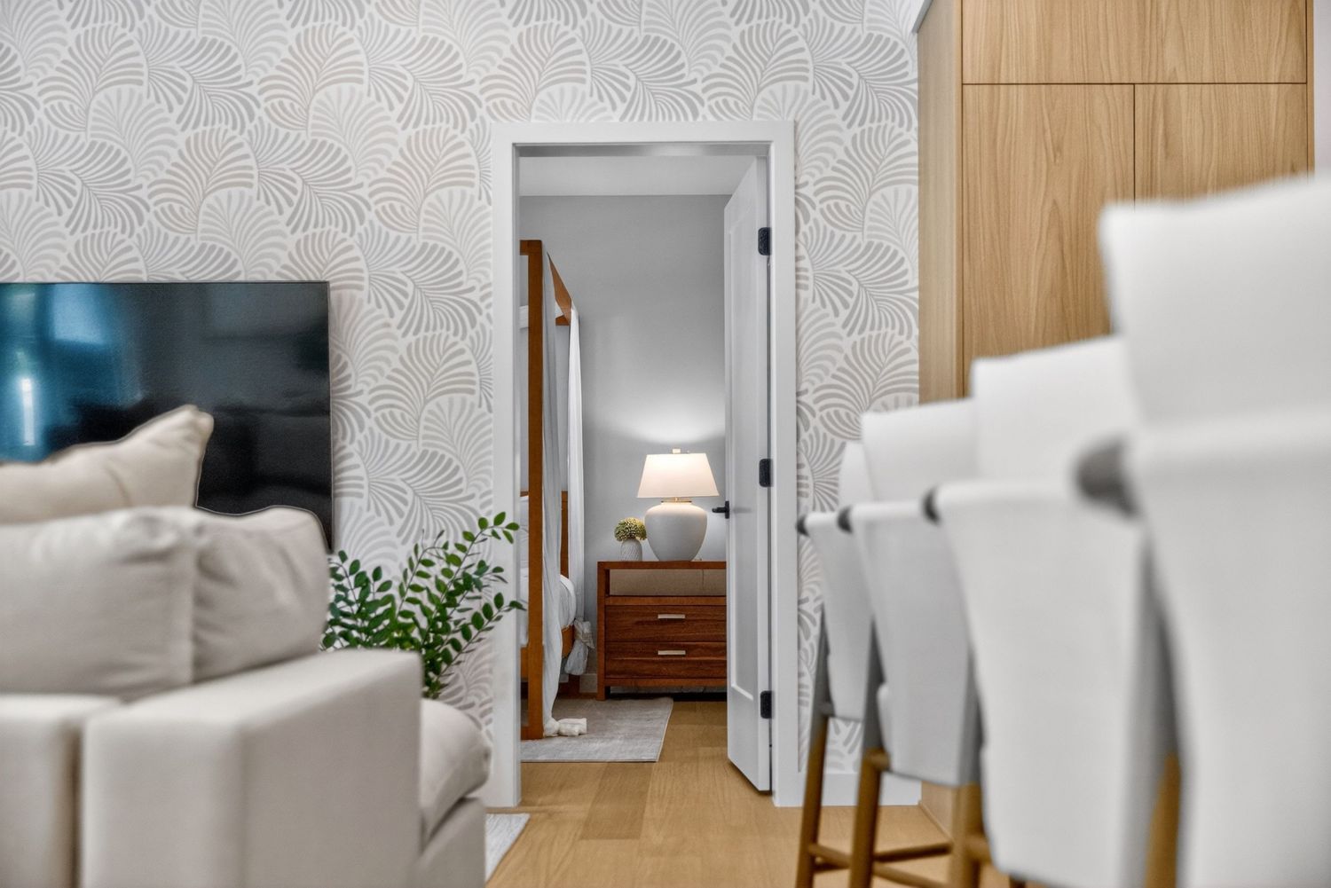 Modern living room with patterned wallpaper, neutral sofa, and hallway leading to a cozy bedroom with warm lighting.