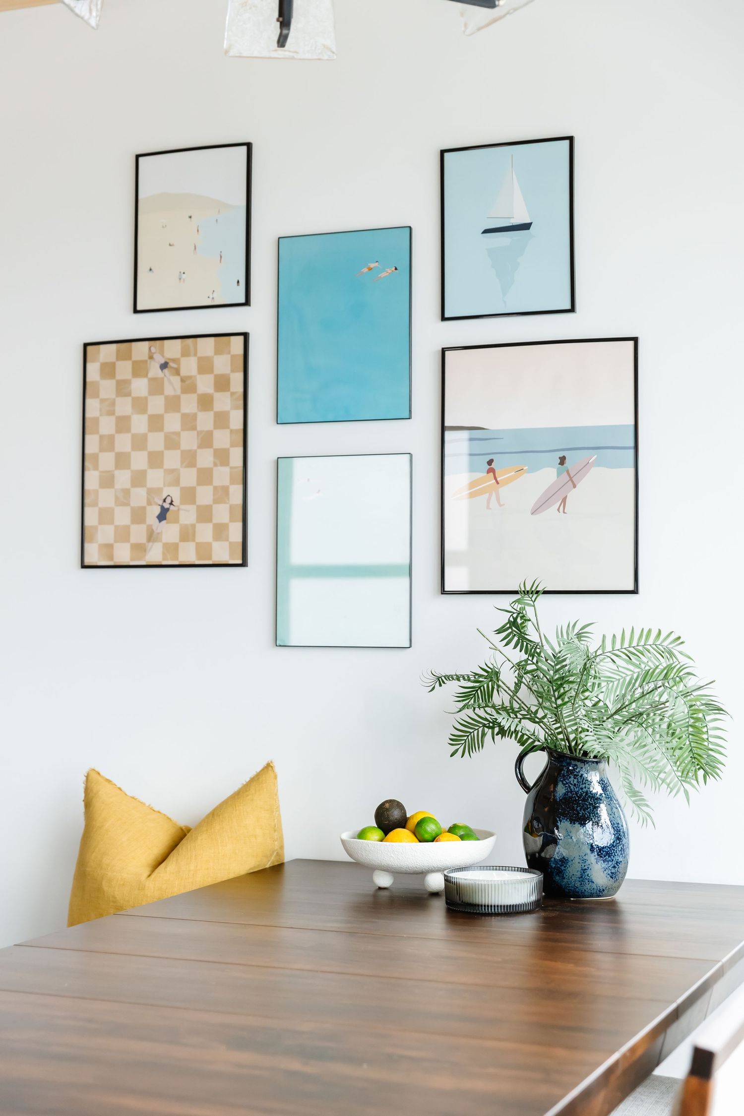 Modern dining room wall features framed abstract art in blue and beige tones above a wooden table with yellow accent pillows