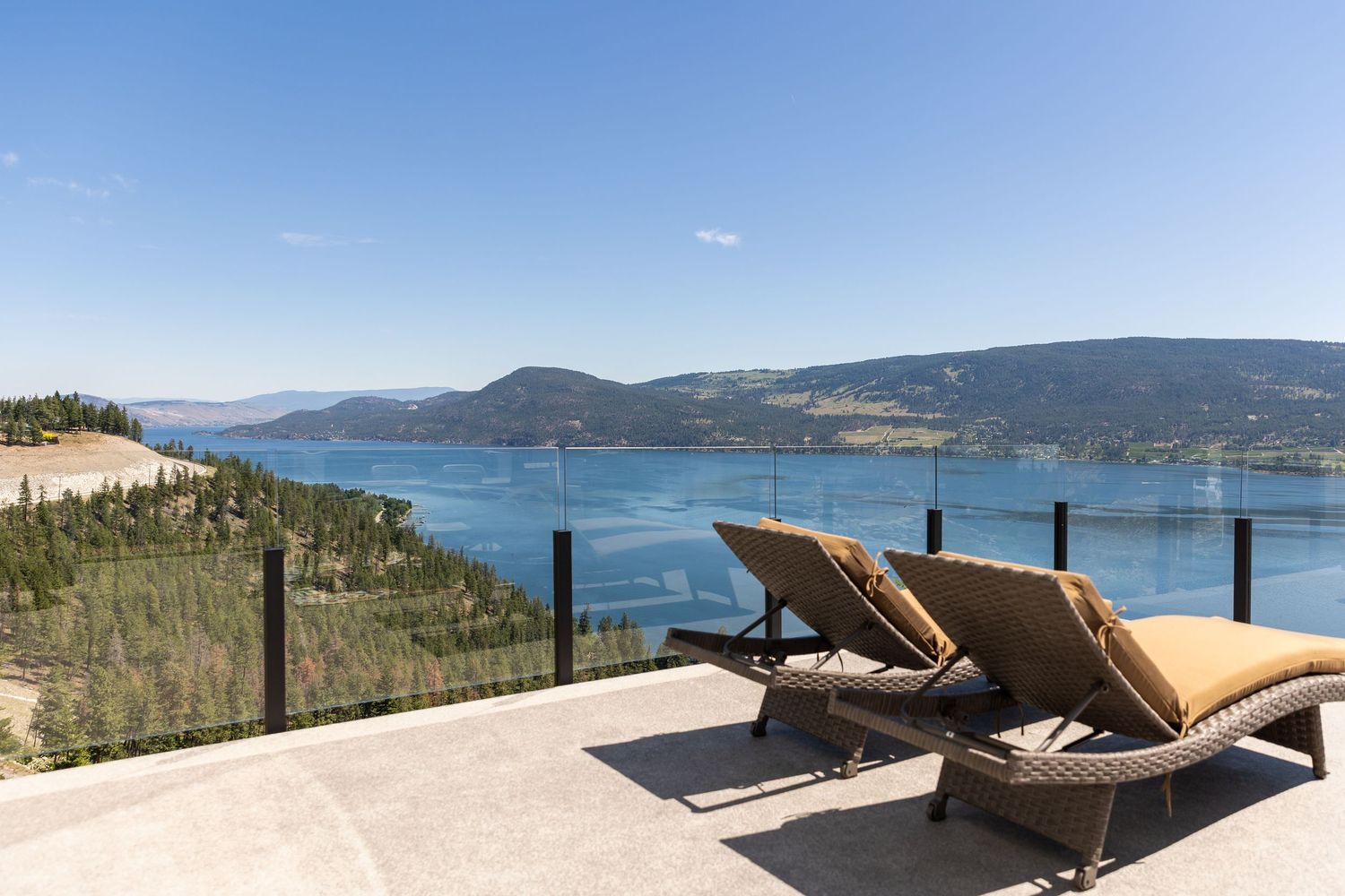 Two lounge chairs overlooking a scenic mountain lake view from a luxury deck with view of Okanagan Lake at airbnb photoshoot