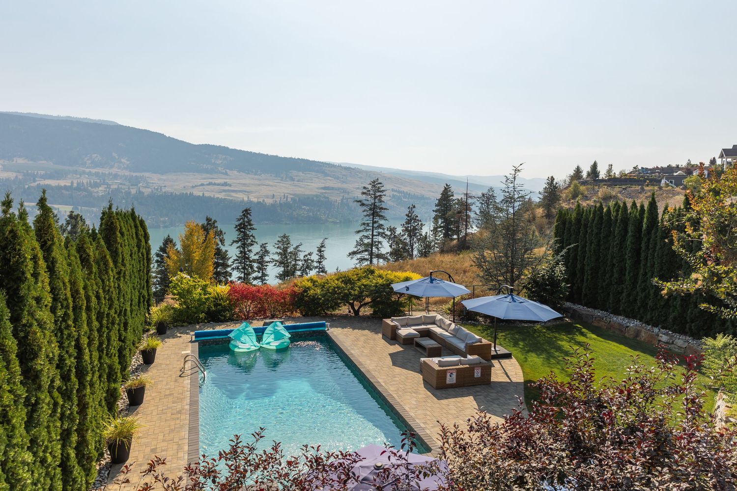Panoramic view of an infinity pool overlooking scenic mountain landscapes and Okanagan Lake in British Columbia.