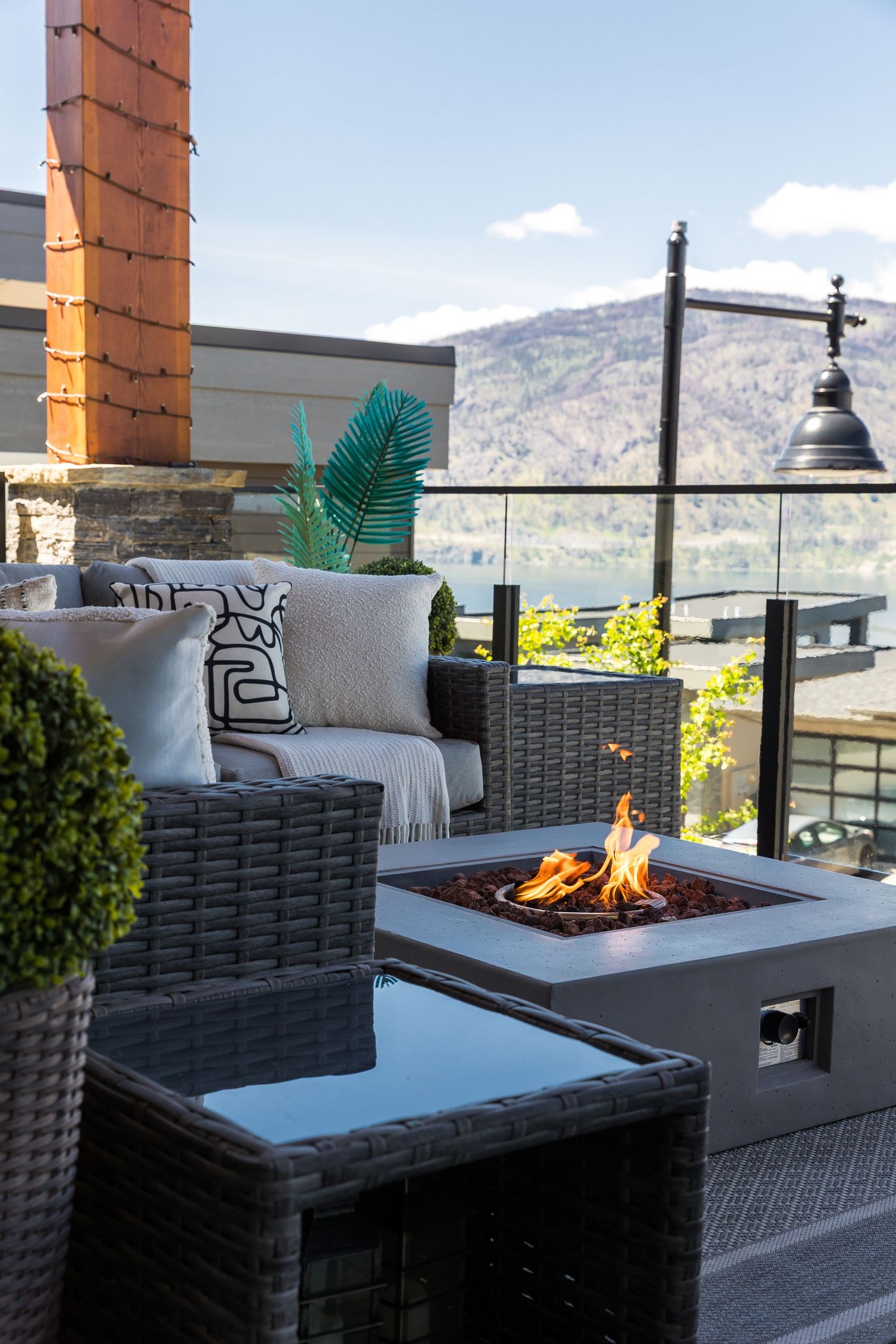 Modern outdoor patio seating area with grey wicker furniture and built-in fire pit overlooking mountain views in a west Kelowna Airbnb