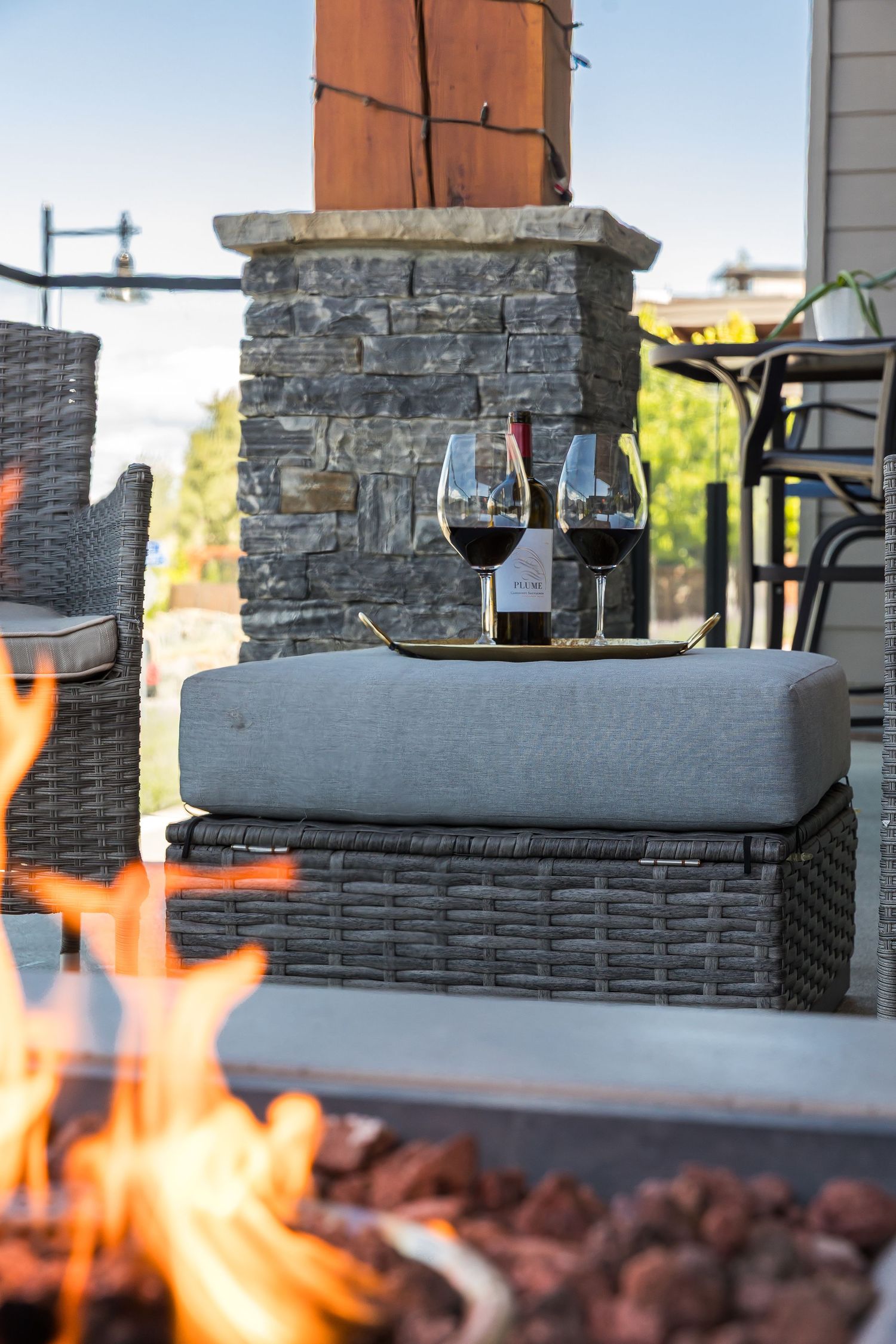 Close-up view of outdoor fire pit with grey cushioned seating and mountain landscape in background in a west Kelowna Airbnb