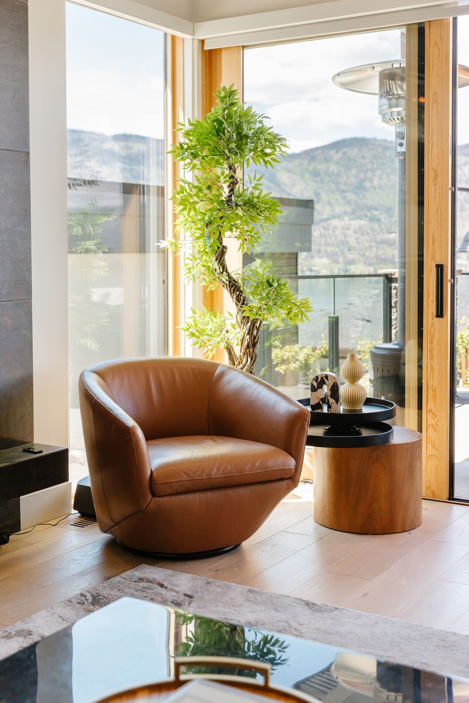 Contemporary living room with brown leather swivel chairs and floor-to-ceiling windows showcasing mountain views in a west Kelowna Airbnb