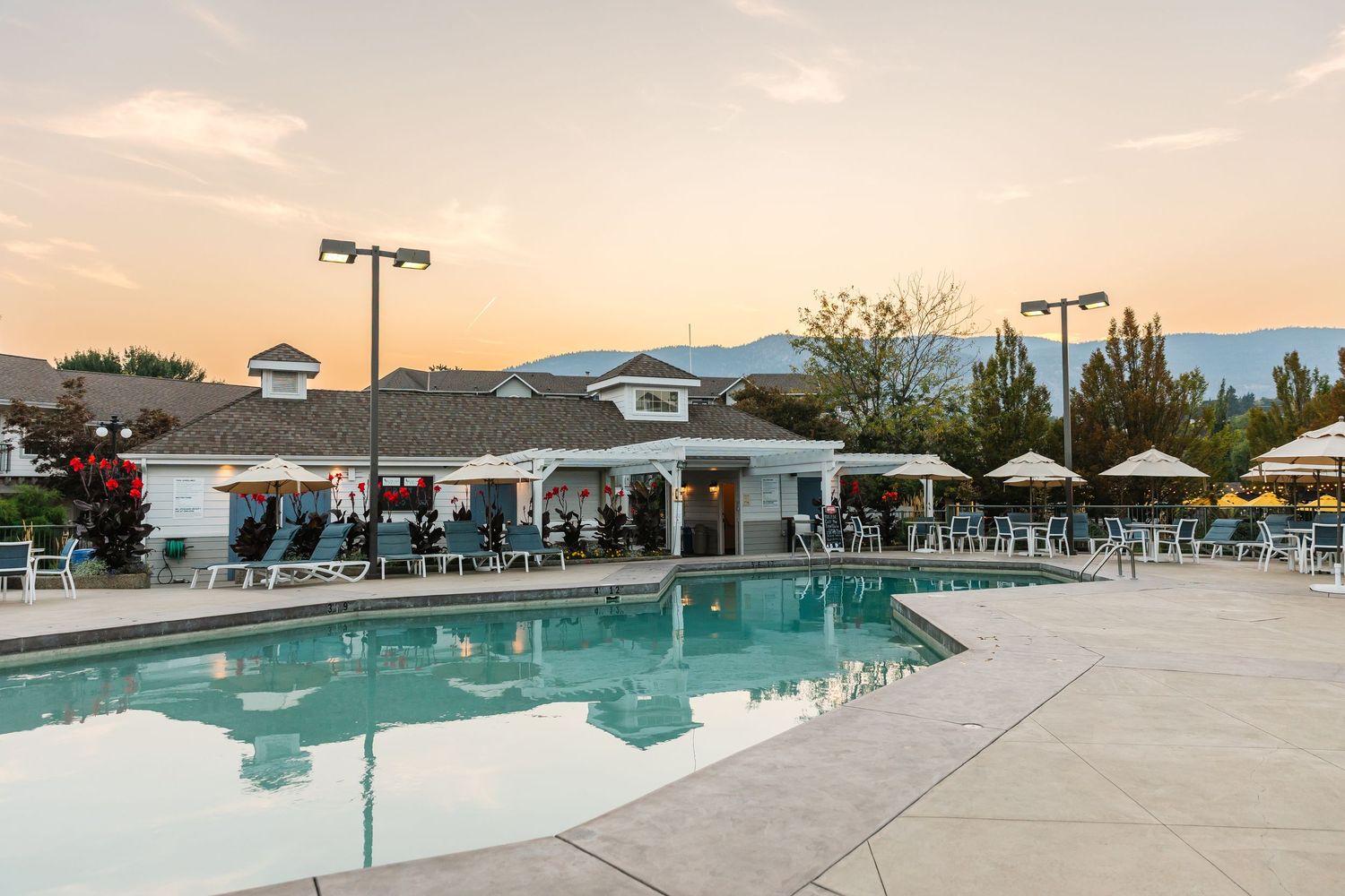 Panoramic view of a resort swimming pool with lounge chairs and mountain backdrop at sunset.