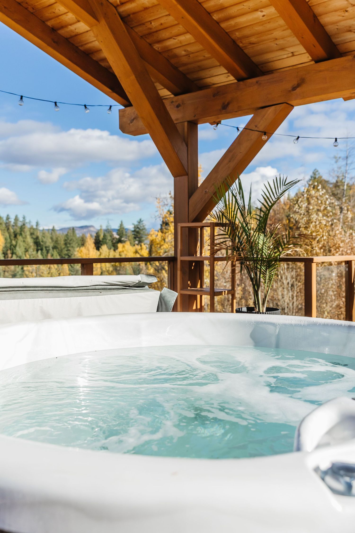 Luxurious outdoor hot tub with steaming water on wooden deck overlooking scenic mountain landscape and autumn trees.