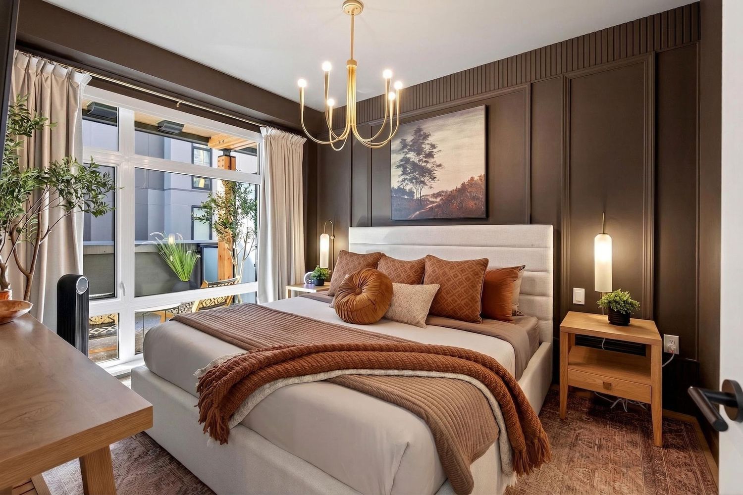 Elegant bedroom with gold chandelier, dark wood paneling, warm earth tones, and terrace access.