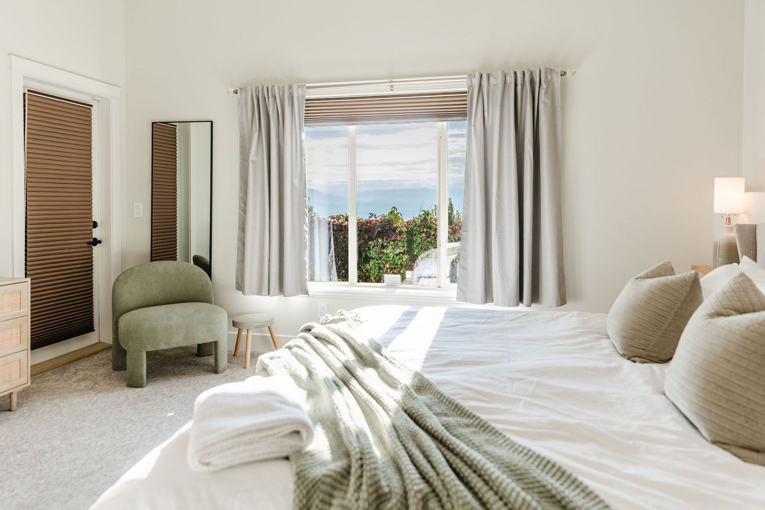 Bright and airy coastal bedroom with white bedding, natural wood elements, and sheer curtains filtering sunlight.