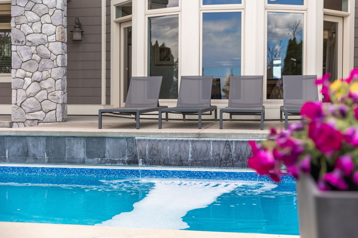 Luxury outdoor pool area with stone facade and pink flowers in foreground.