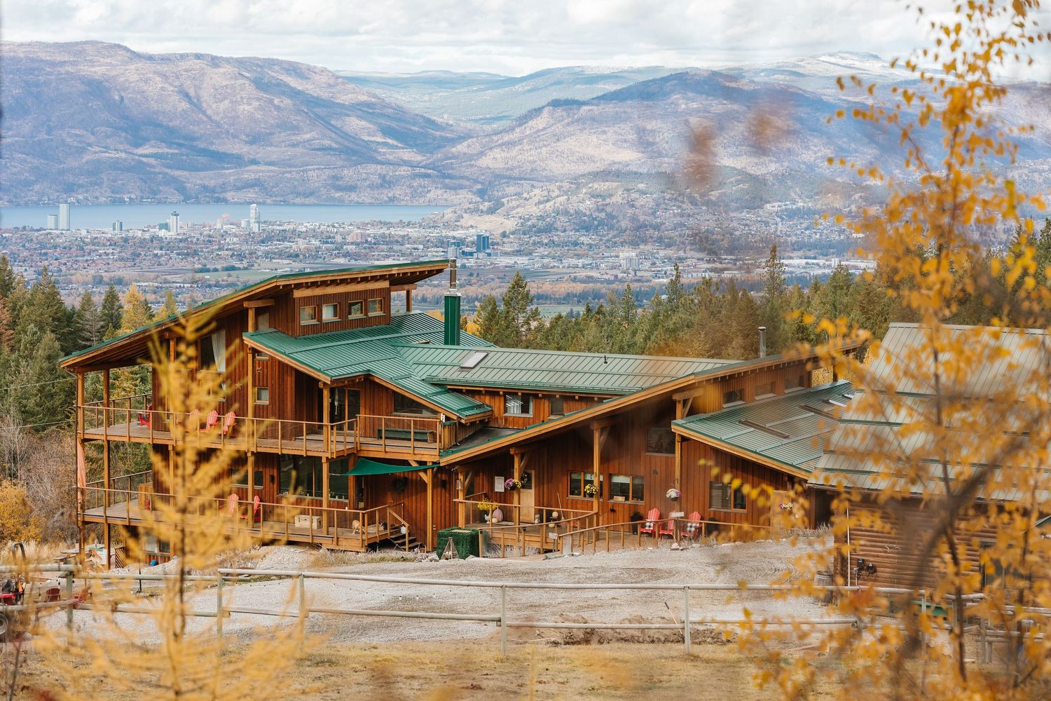 Scenic mountain landscape with rustic wooden lodges nestled among autumn trees overlooking a distant valley and city.