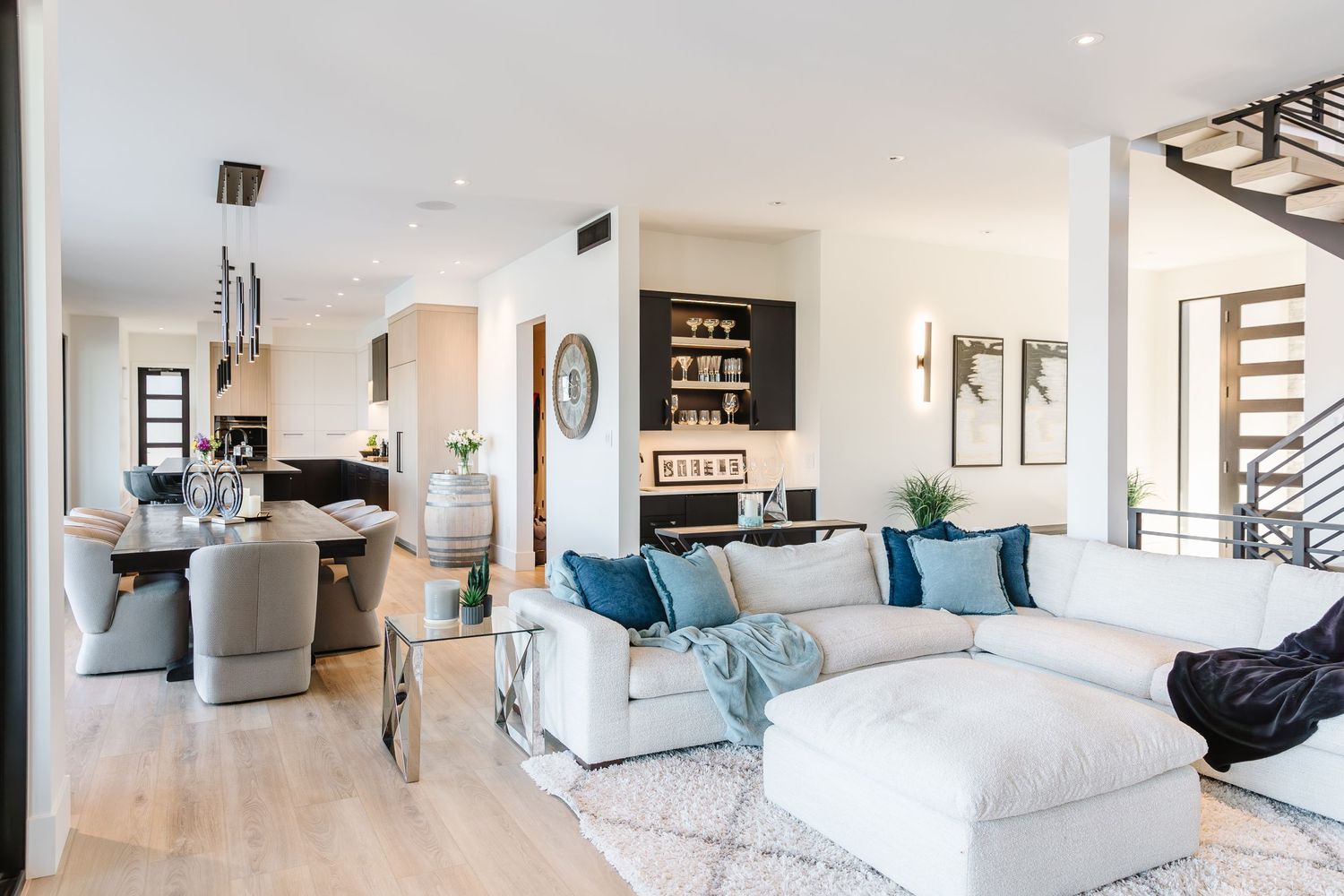 Modern open concept living room with white and blue decor featuring plush seating and hardwood floors.